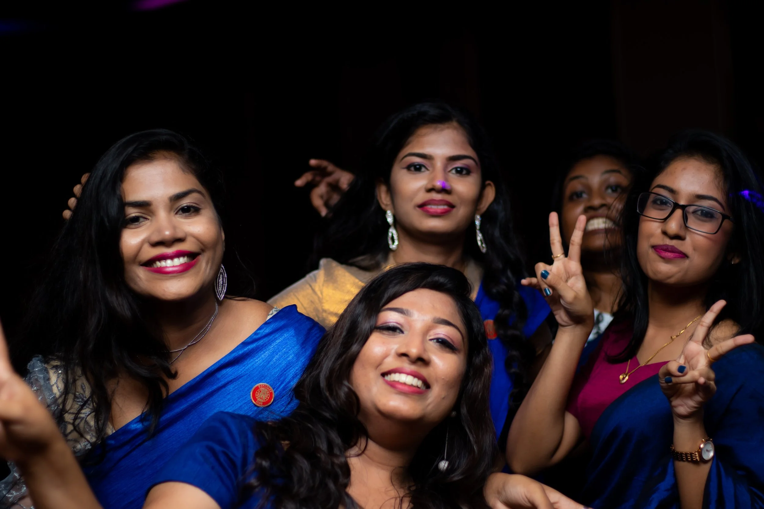 Group of five women smiling and making peace signs at a celebration or party.