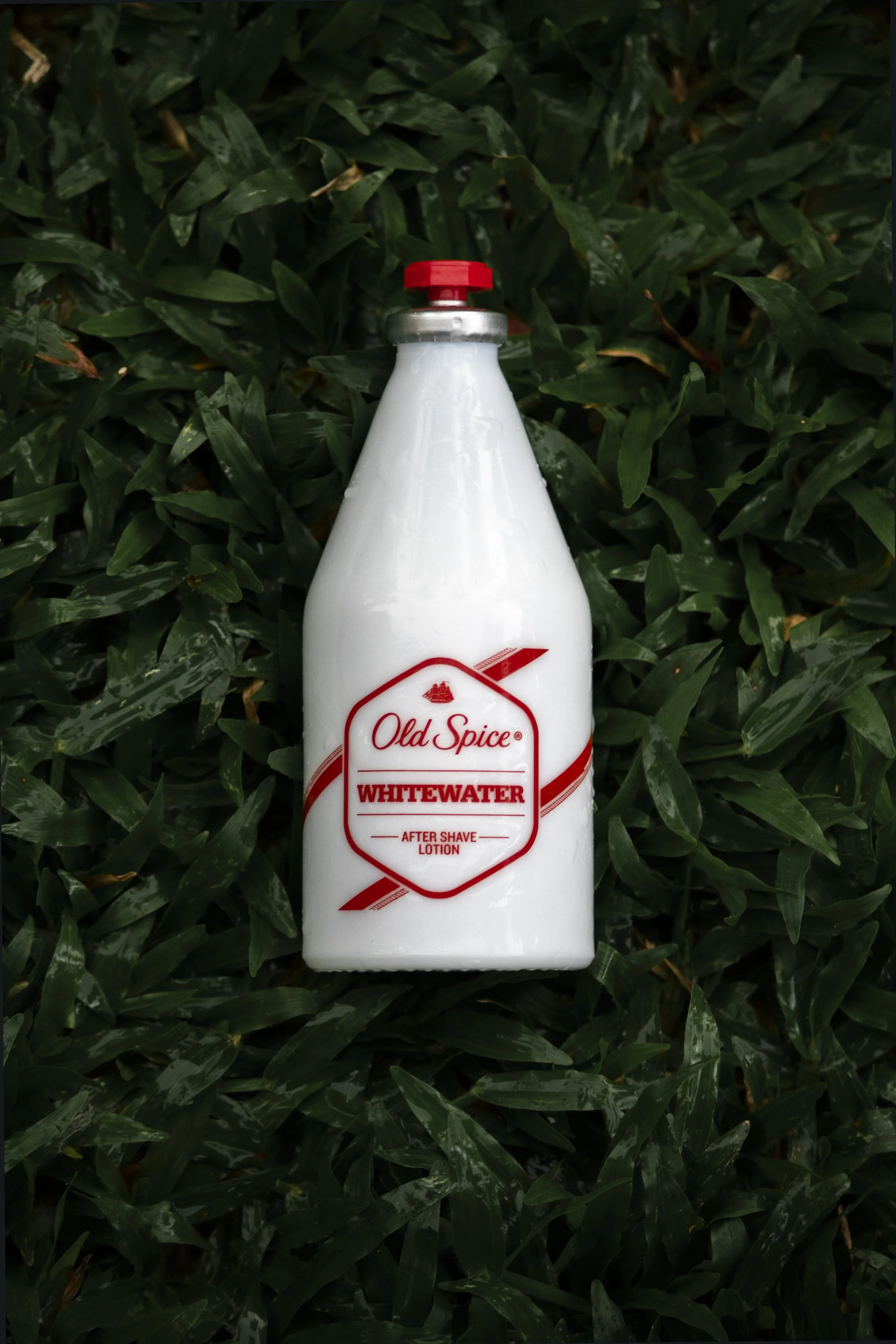 A white bottle of Old Spice Whitewater after shave lotion, placed on green grass.