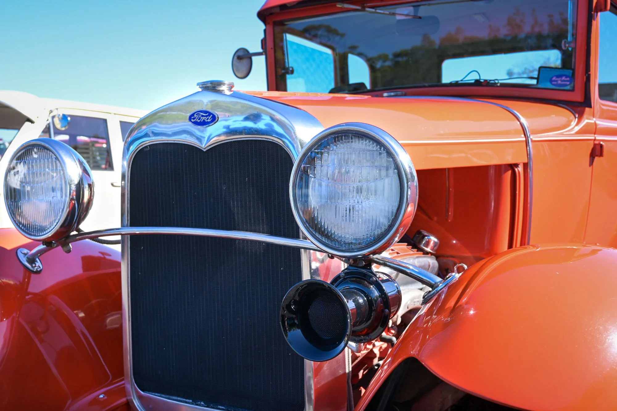 Front view of a vintage orange Ford automobile with chrome headlights and grille, parked outdoors under a clear blue sky.