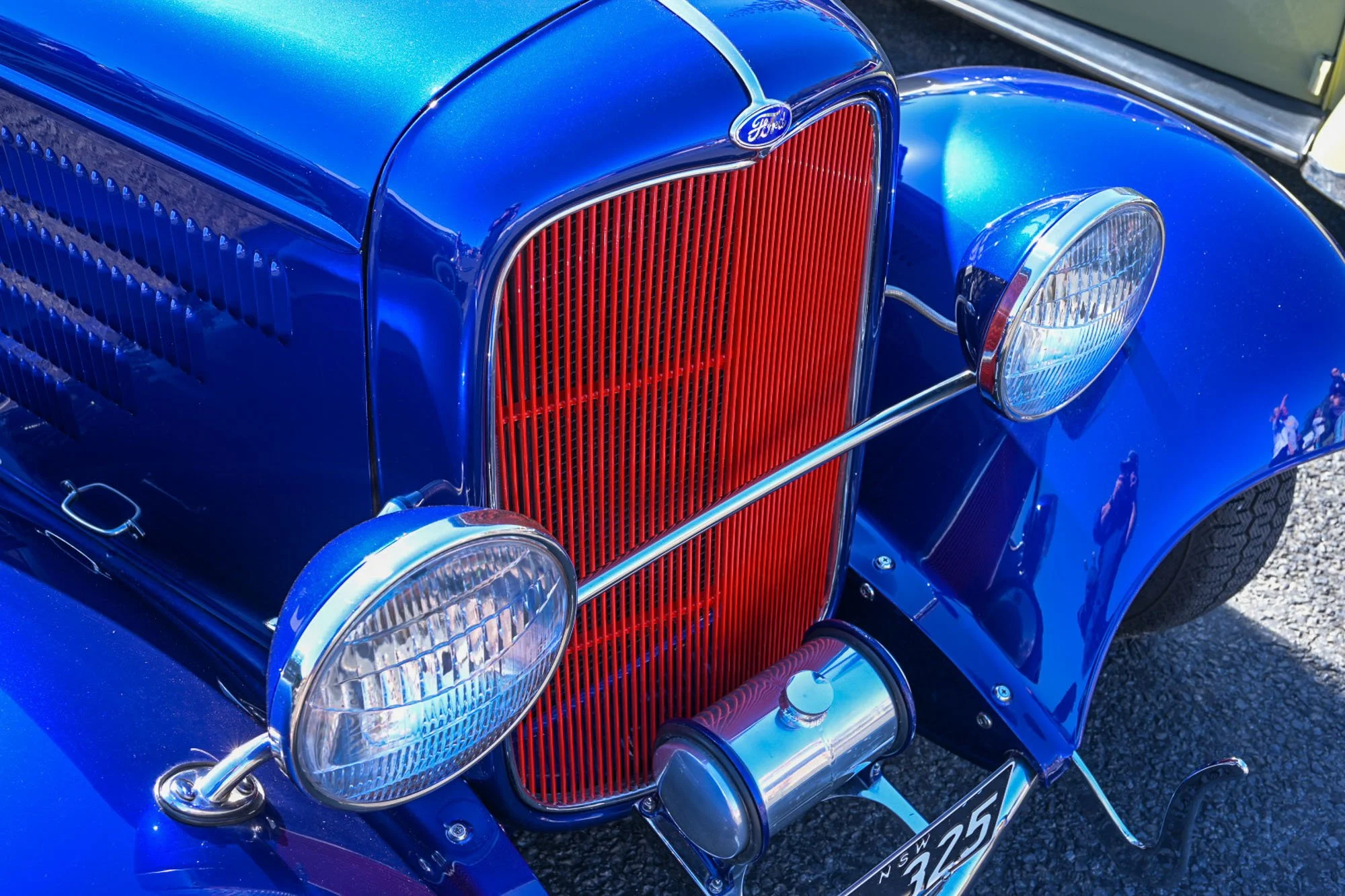 Close-up of a vintage blue Ford car with a prominent red grille, round headlights, and chrome accents.
