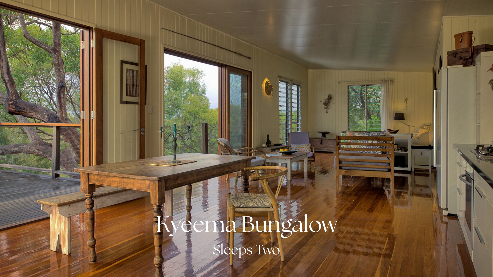 Interior of a cozy living space with wooden floors, a dining table, chairs, and a view of trees outside through large glass doors and windows.