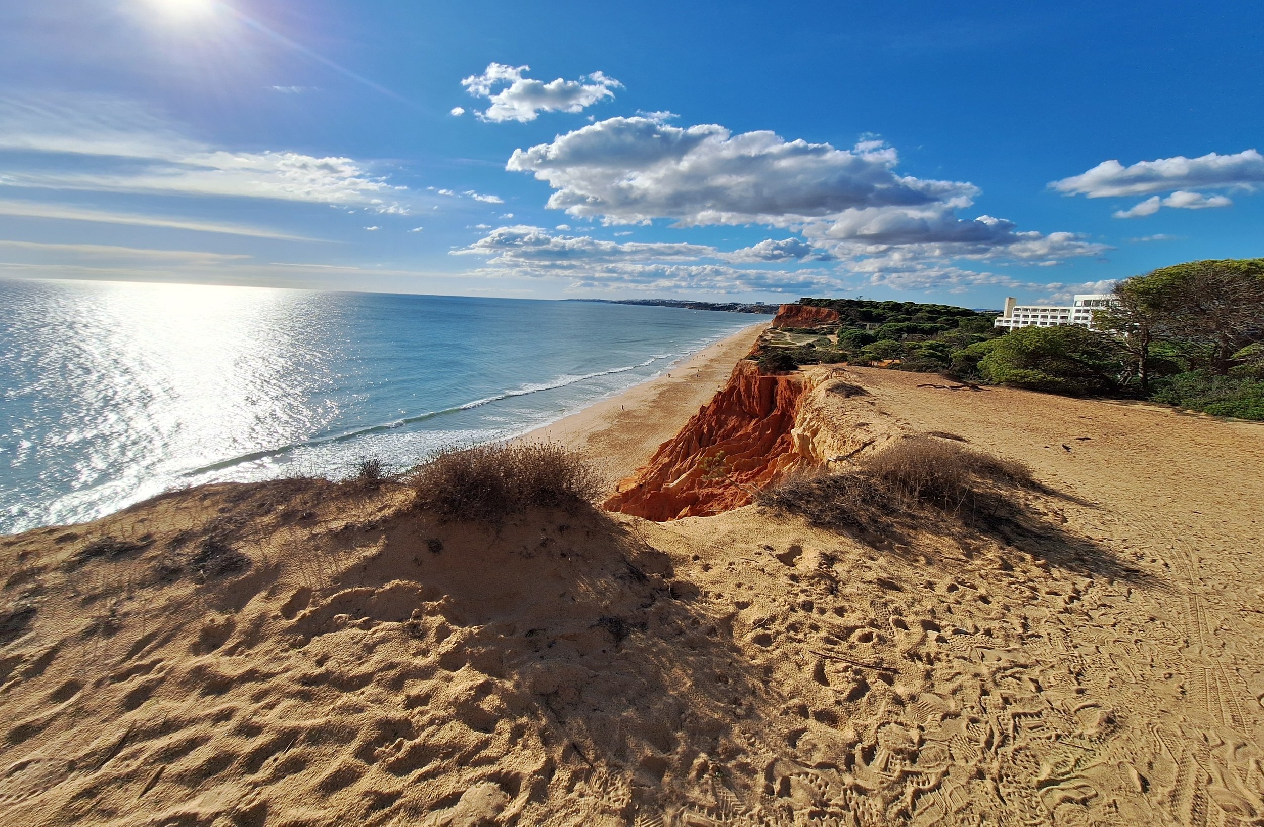Plage de sable avec des falaises rocheuses orange, vue sur l'océan sous un ciel bleu avec quelques nuages.