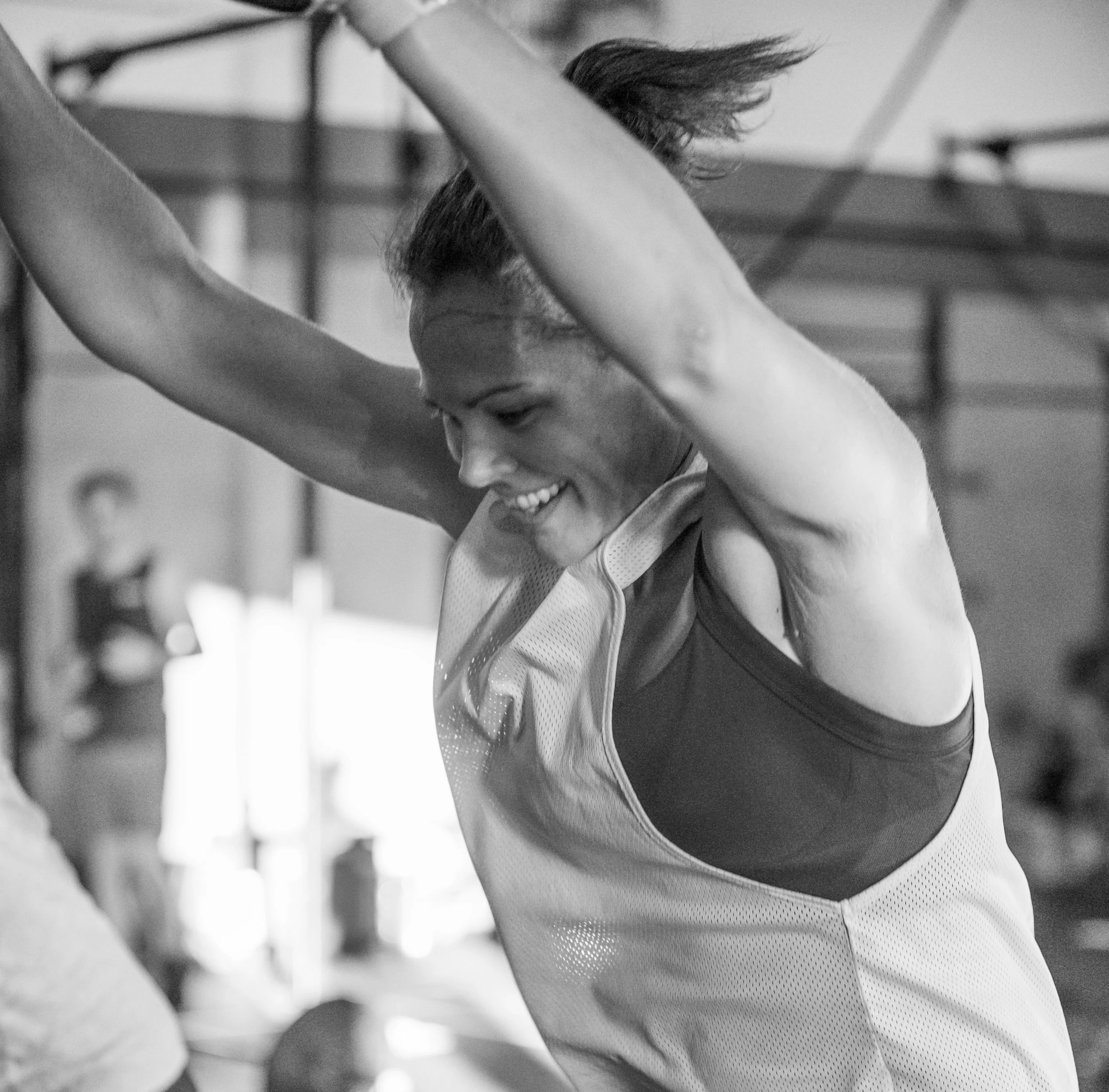 A woman smiling with her arms raised after a workout, wearing athletic clothing in a gym.