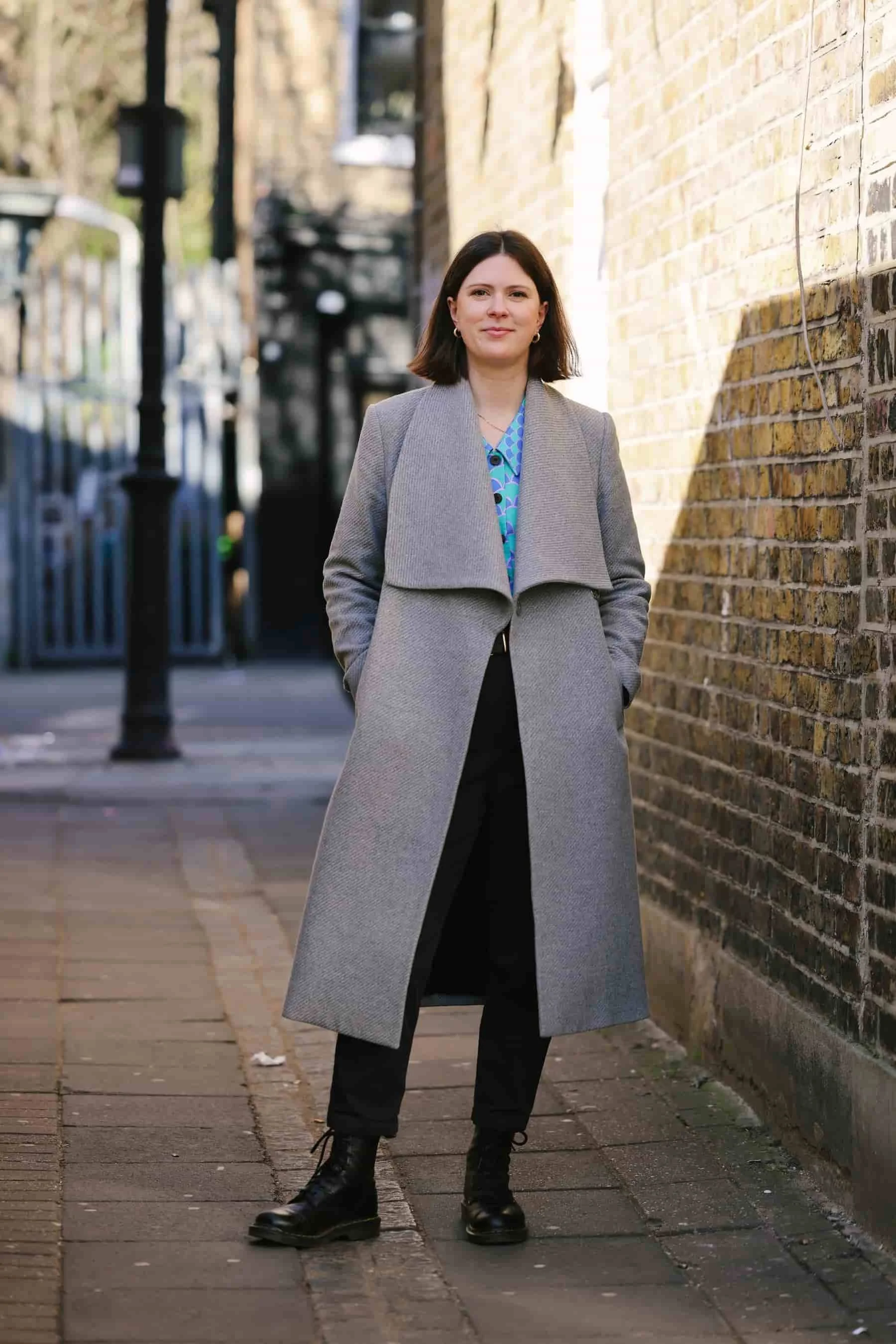 Full length shot of Dr Claire Buky-Webster, clinical psychologist, facing to camera and smiling, standing outdoors near her therapy practice in South London.