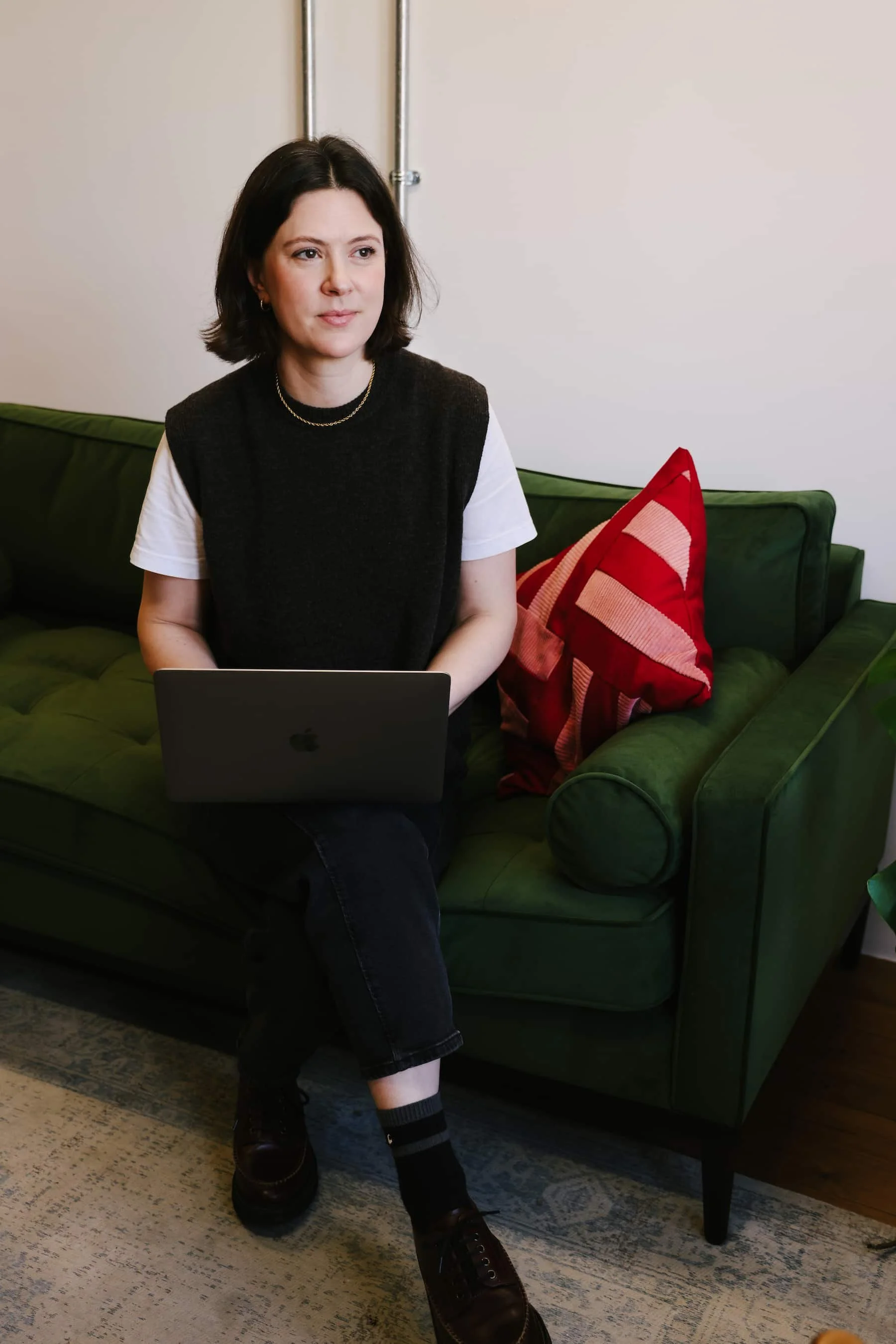 Close-up shot of Claire Buky-Webster sitting on a dark green sofa working on her laptop