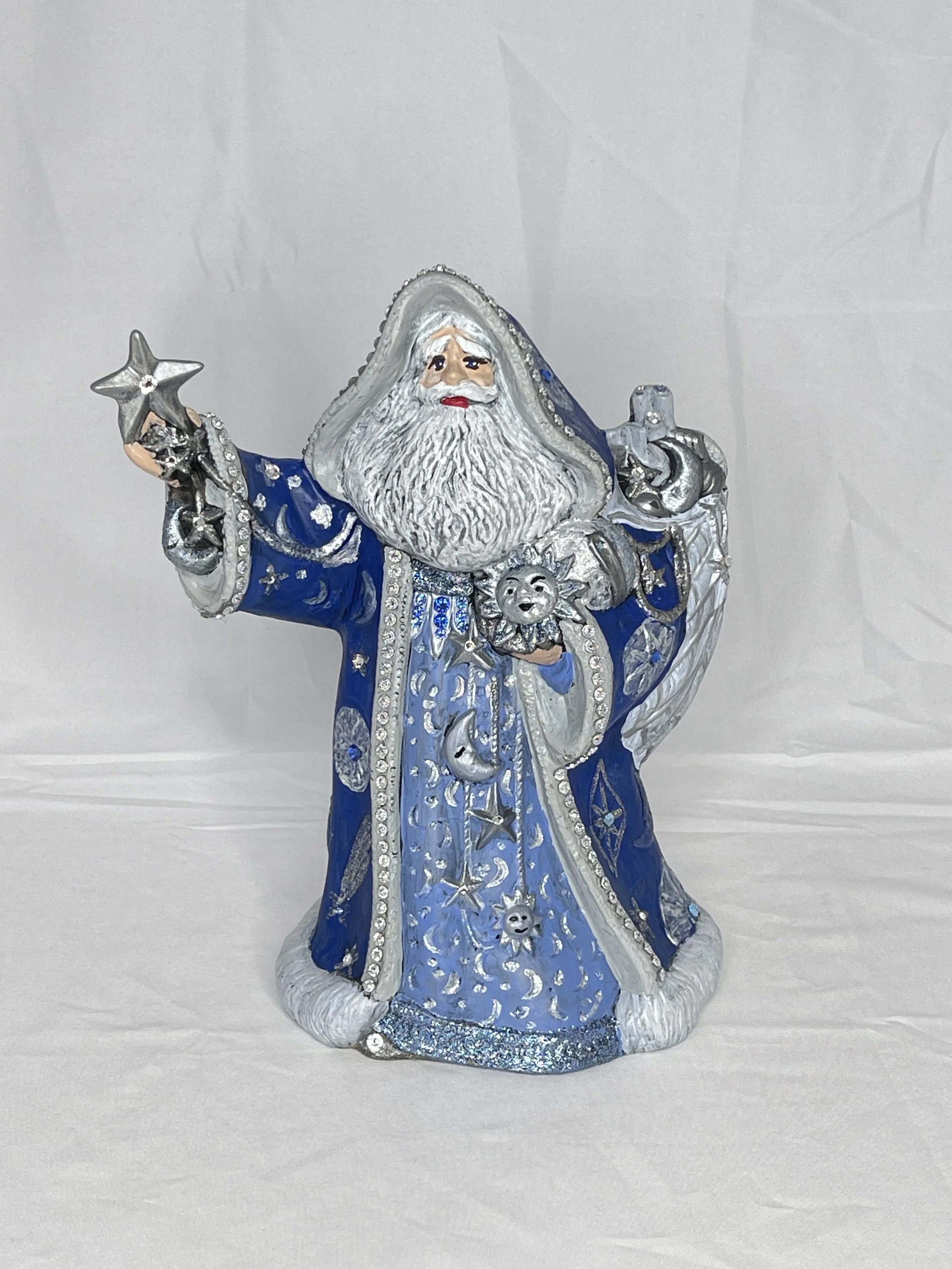 Decorative figurine of a wizard-like Santa Claus with a long beard, wearing a blue robe and holding a star, a sun, and a moon.