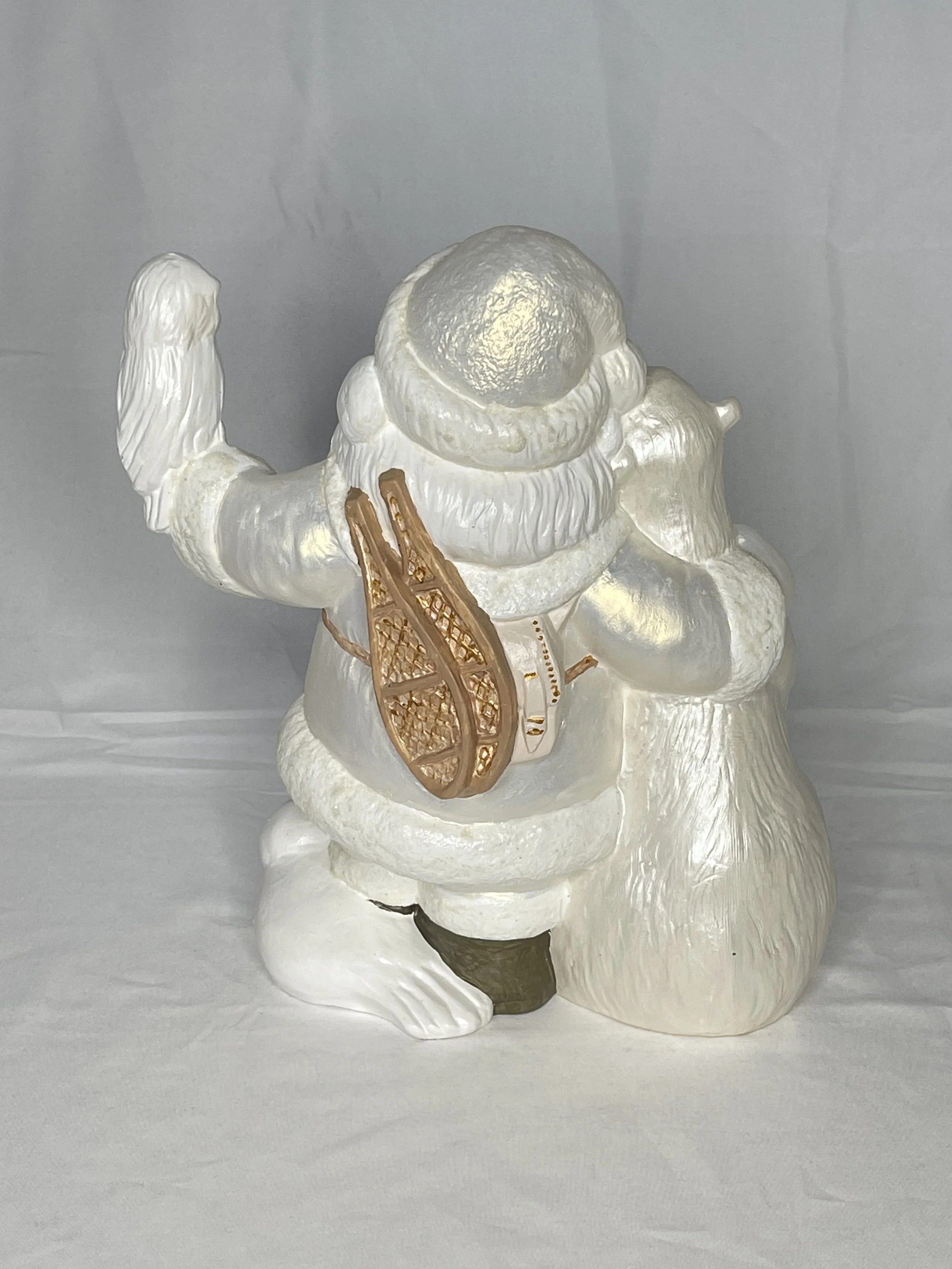 White ceramic Santa Claus figurine with a gold sled and a brown gift bag, sitting on a white surface with a light gray background.