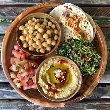Wooden platter with hummus, chickpeas, diced tomatoes, tabbouleh, and pita bread.