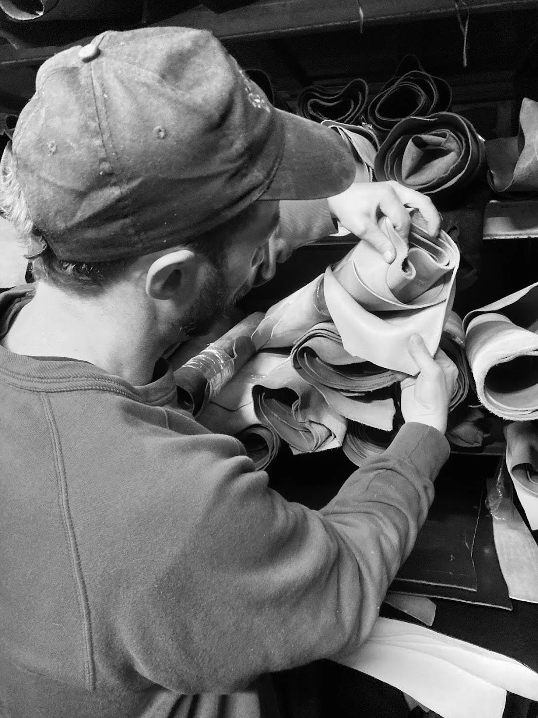 A man wearing a cap and sweatshirt folding or inspecting fabric or paper rolls at a workbench.