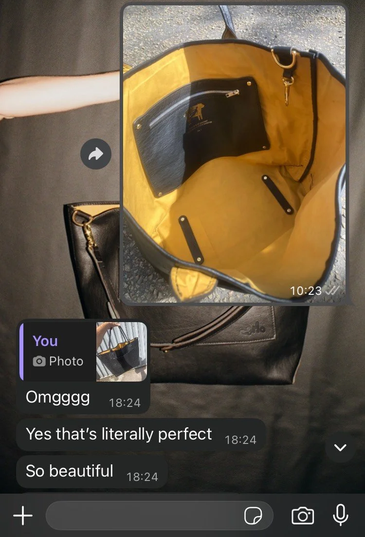 A yellow tote bag with black interior, including a zippered pocket, on top of a black Louis Vuitton bag. Inside the tote, there are black straps and at the bottom, a black Louis Vuitton bag with a zipper and gold hardware is partially visible. The conversation on the screen shows someone expressing admiration for the tote bag.