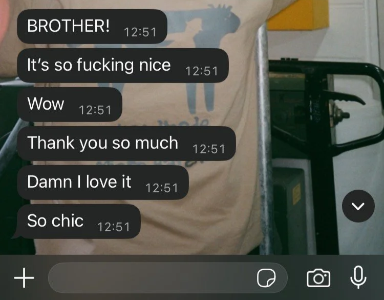 A close-up of a beige T-shirt with a blue giraffe graphic, hanging on a hanger, with black text messages overlaid on the image.