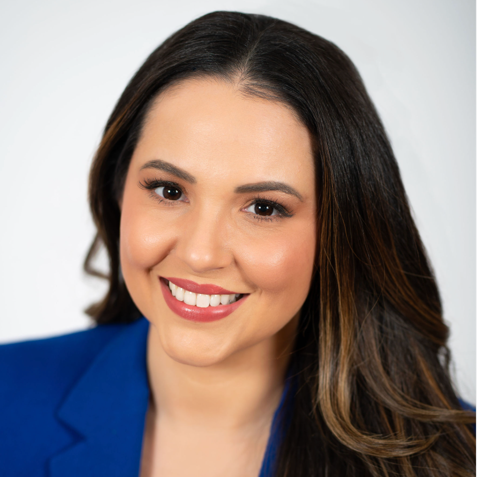 A parenting influencer with million followers  with long dark hair wearing a blue blazer, smiling against a plain light background.