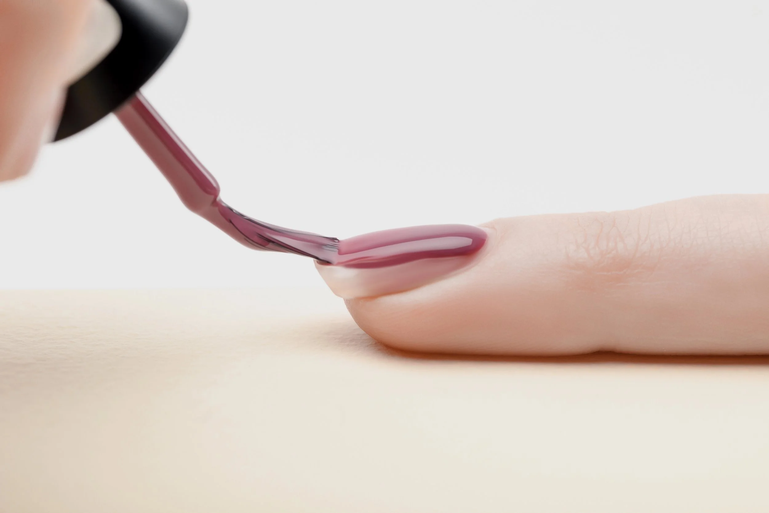 Close-up of a person applying pink nail polish to their thumbnail with a brush.