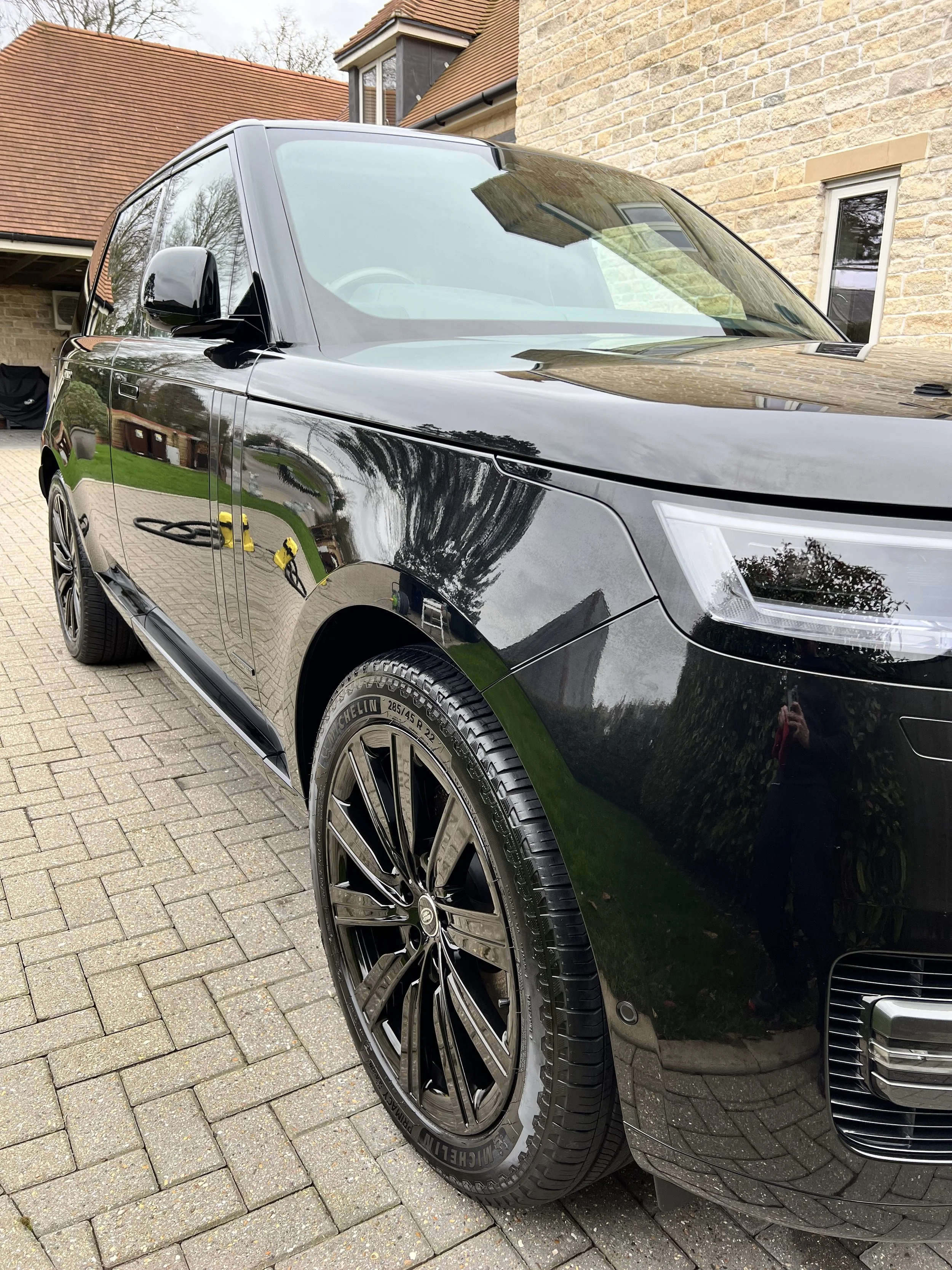 Close-up of a black luxury car parked on a brick driveway in front of house with brick walls and windows