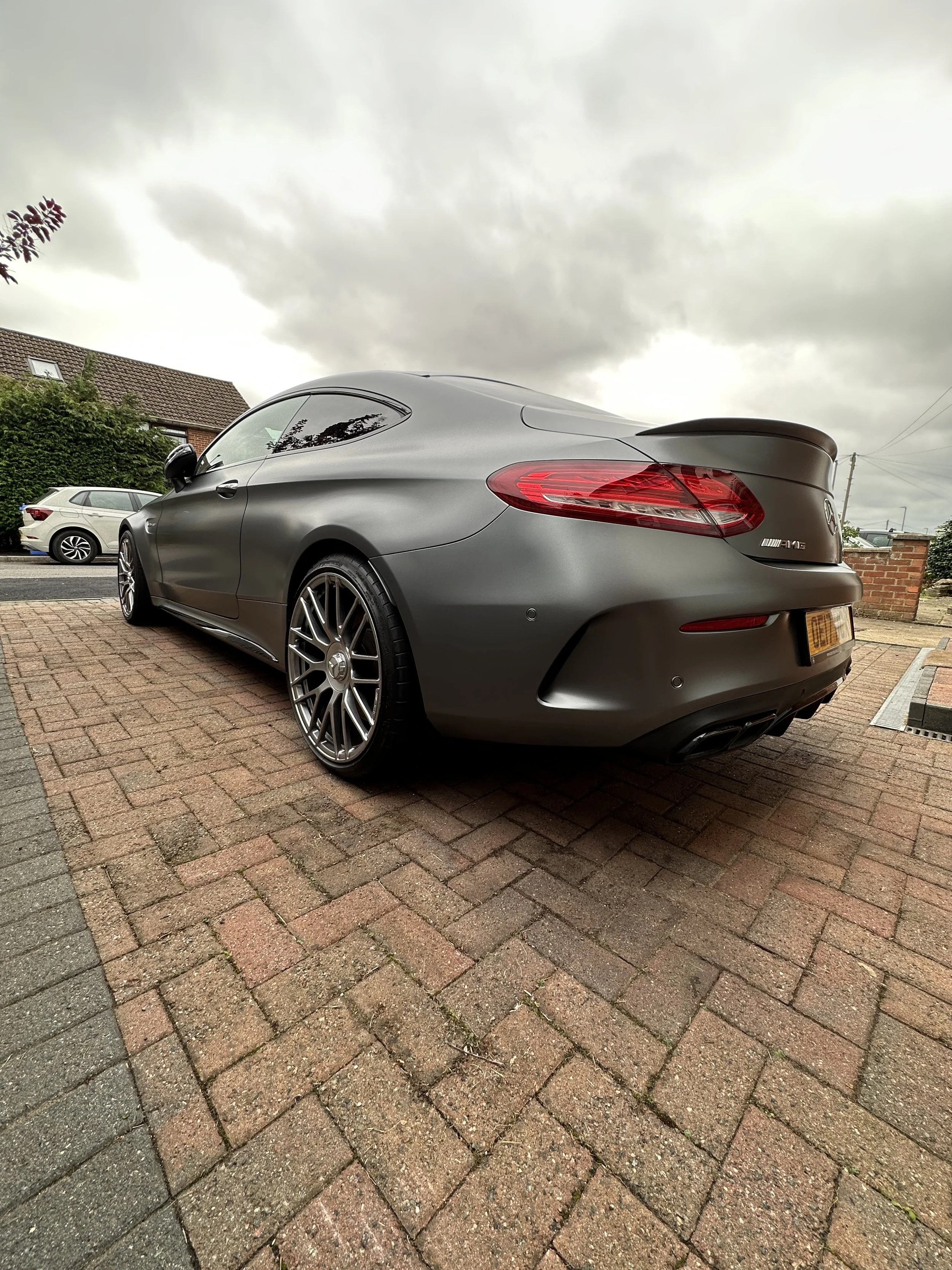 Gray Mercedes-Benz coupe parked on brick driveway under cloudy sky