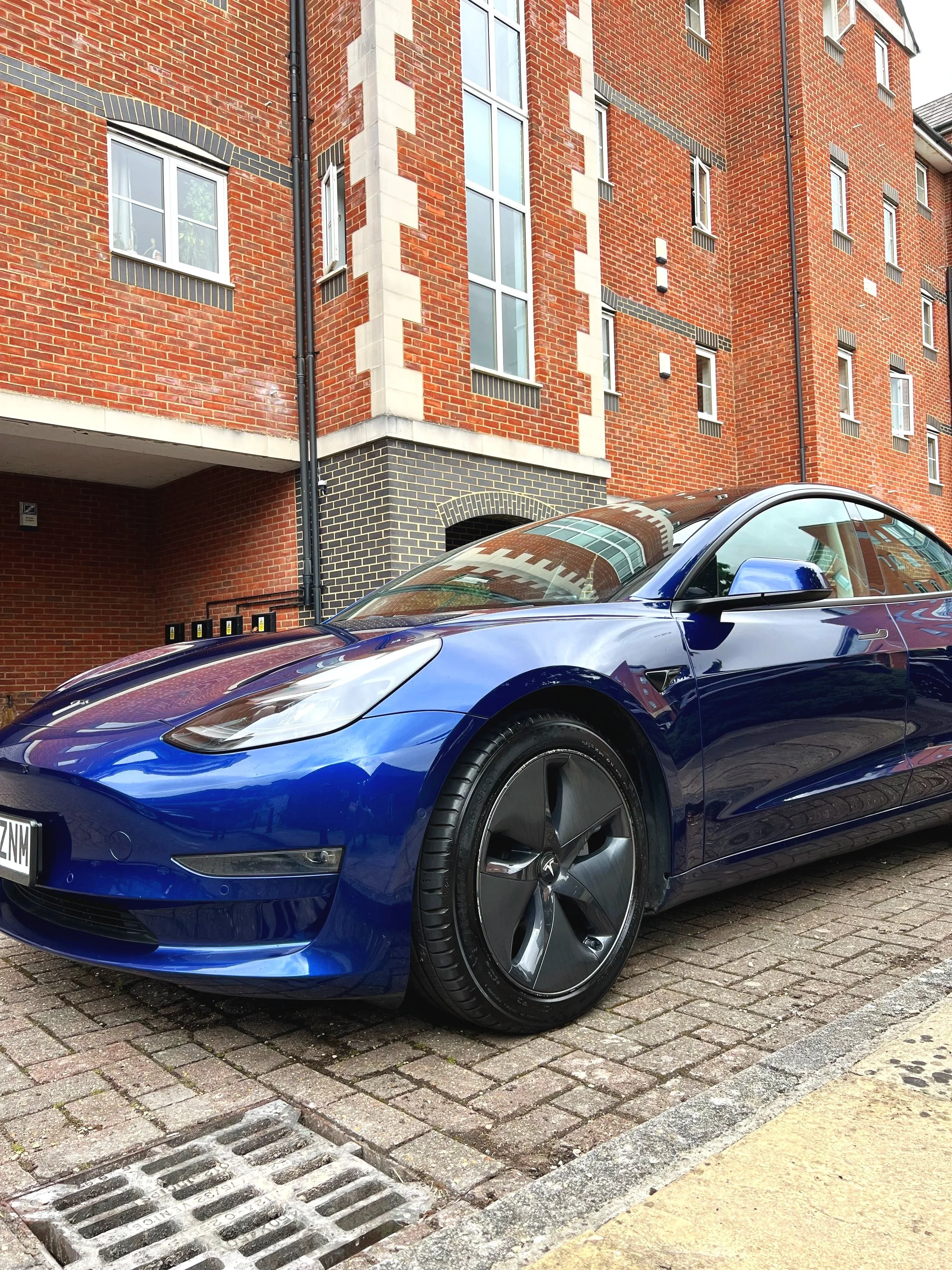 A sleek blue electric car parked on a brick street in front of a red brick building with multiple windows after full mobile valet and detailing.