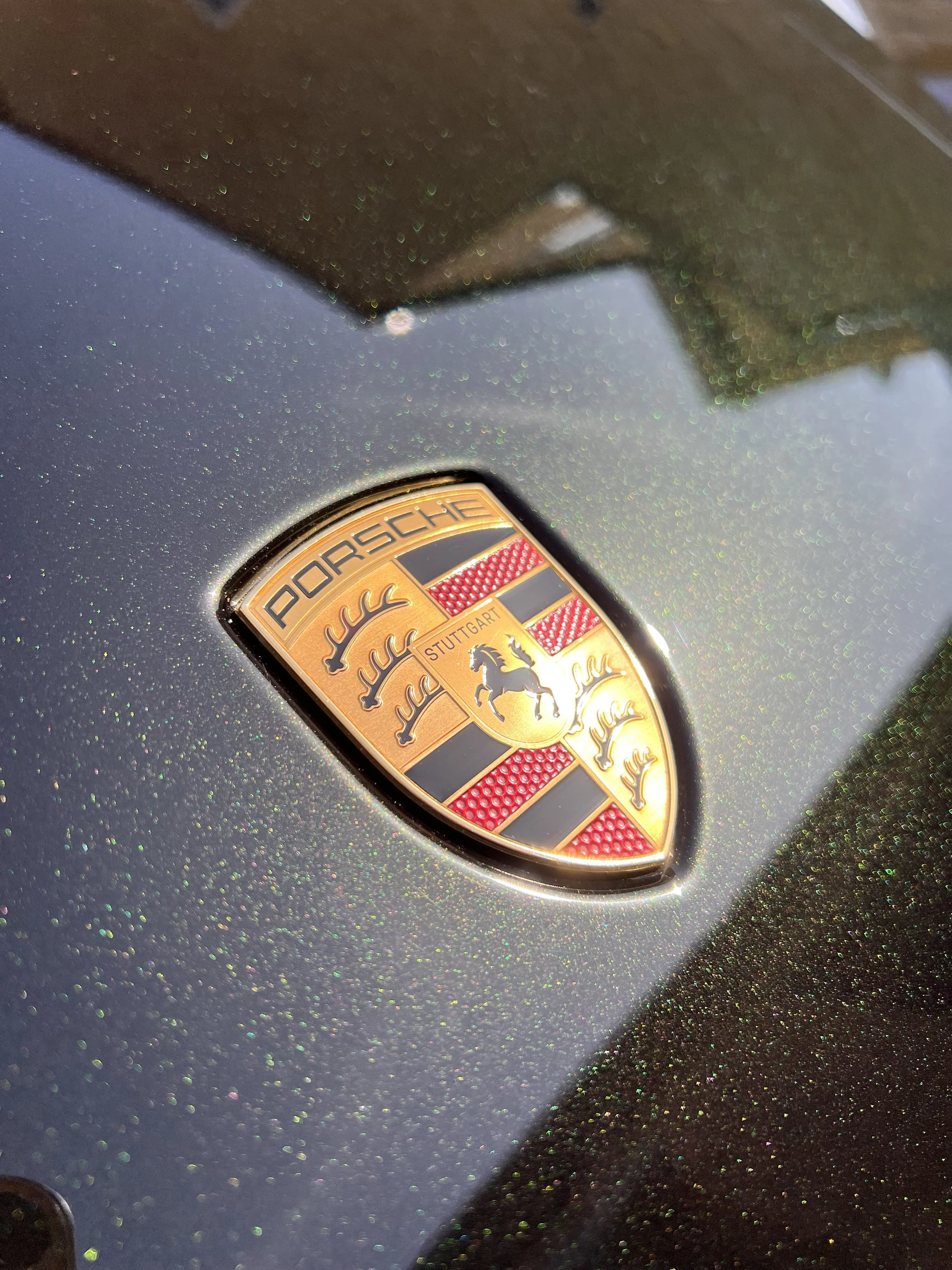 A close-up of a black Porsche vehicle with a sparkly, glittery finish and the Porsche emblem logo.