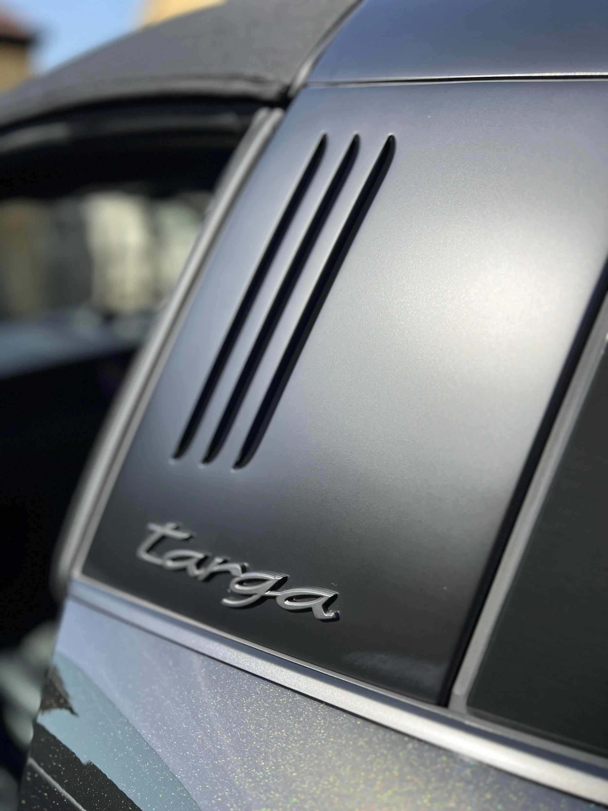 Close-up of a silver car's hood with black vents and a silver badge that reads 'Targa'.