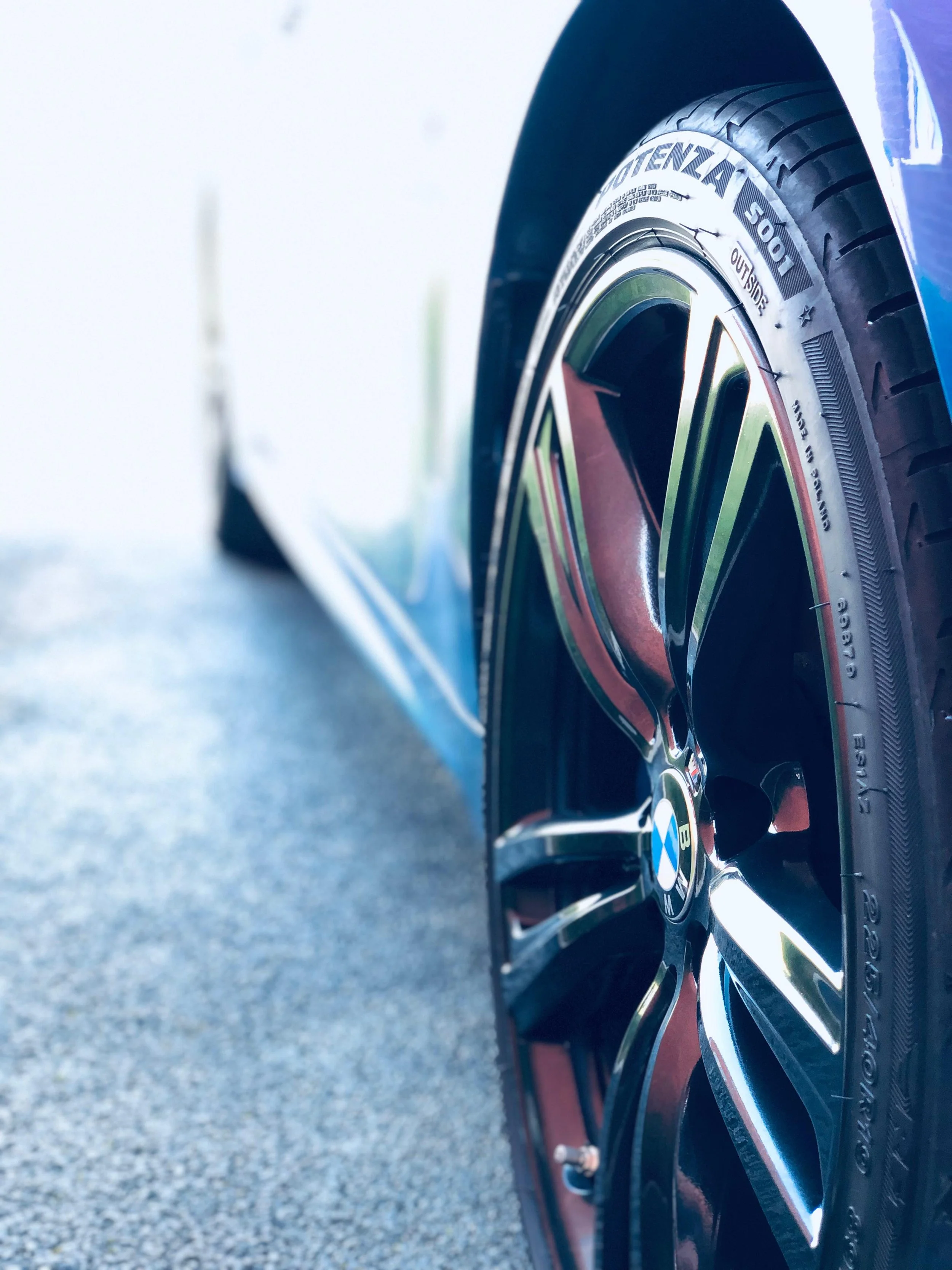 Close-up of a BMW car tire and wheel with a black and silver rim, parked on a concrete surface.