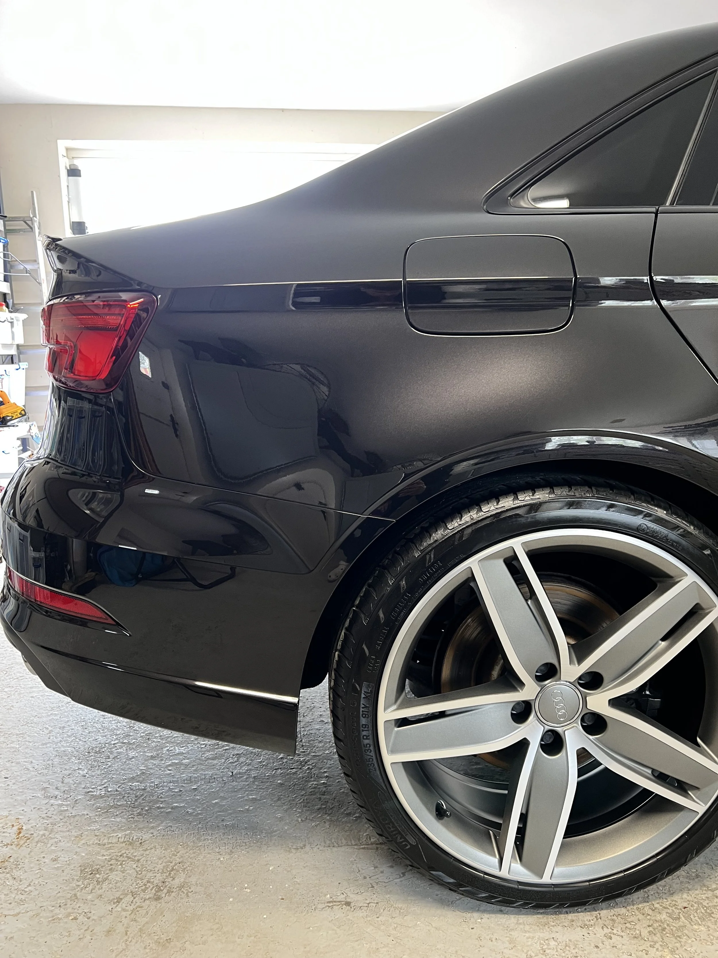 Rear side of a black Audi car parked in a garage after full valet and detail and ceramic coating.