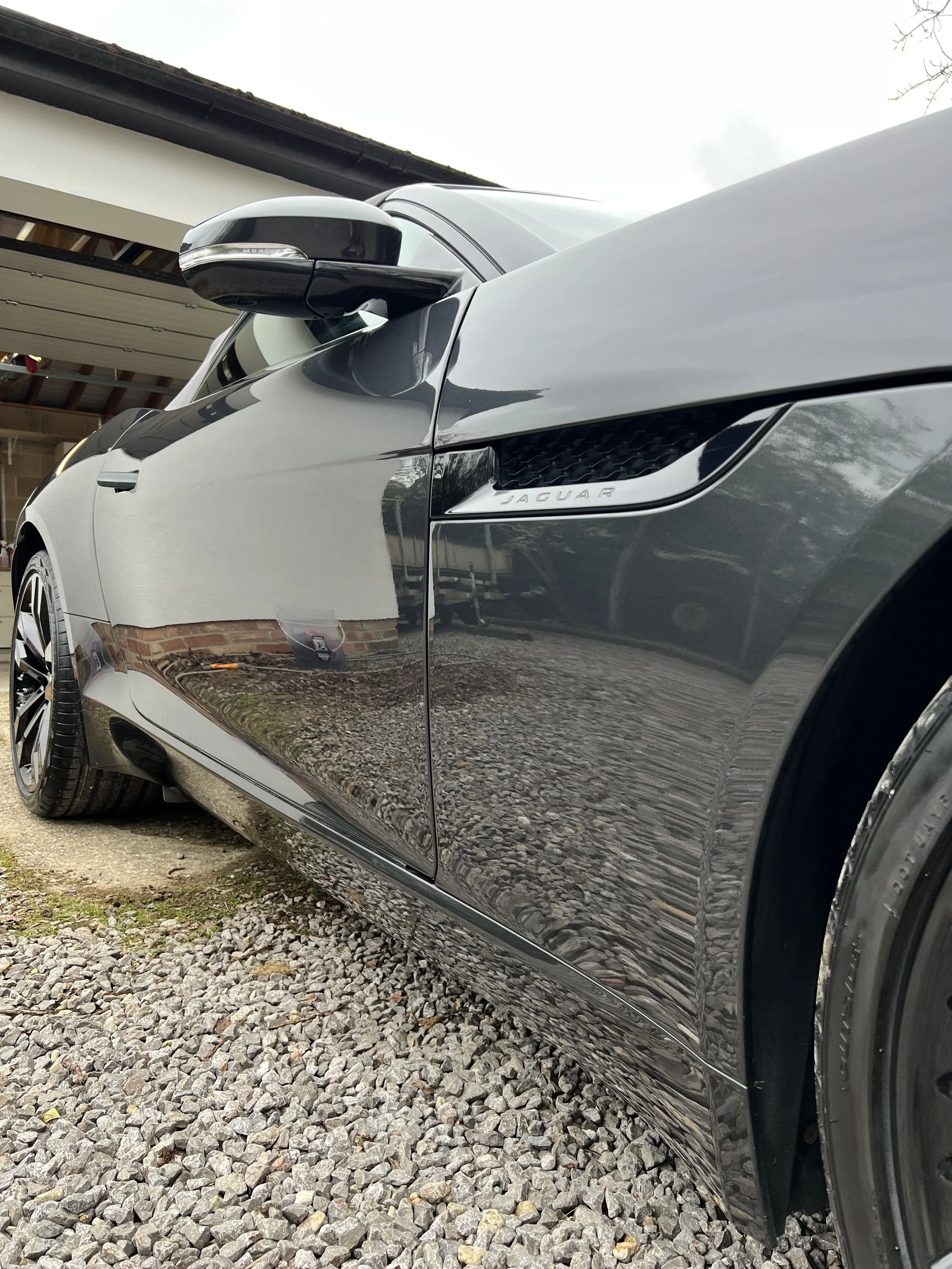 Close-up of a black luxury Jaguar car parked on a gravel driveway, with a building in the background.