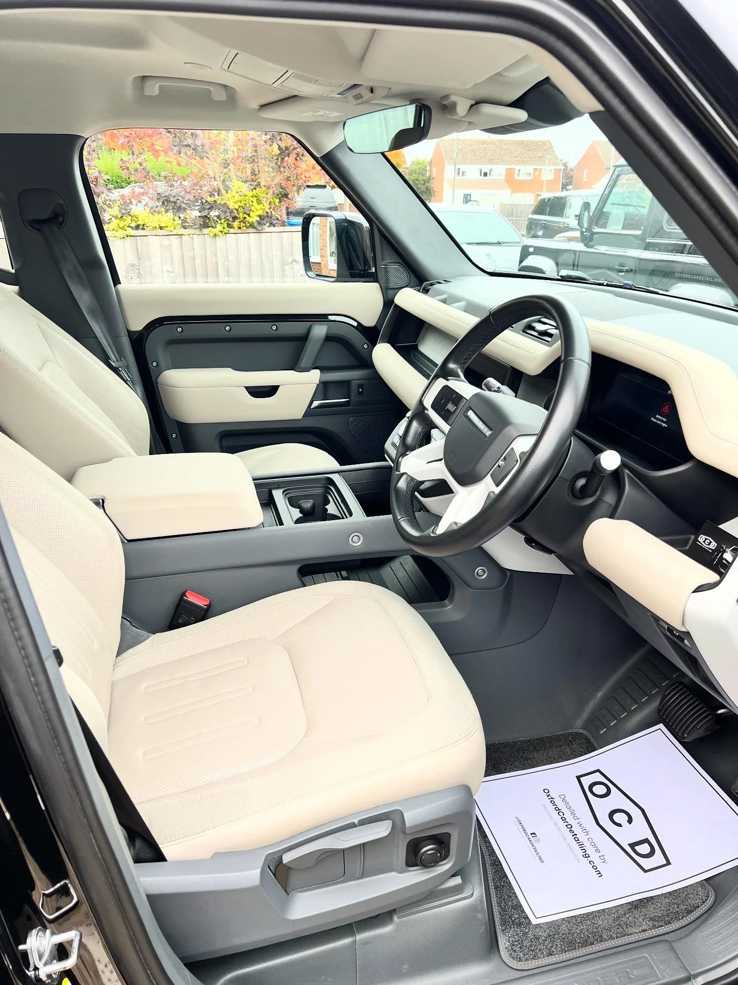 Interior view of a vehicle showing a beige front passenger seat, a black steering wheel, and dashboard, with a paper mat on the floor that reads 'OCD' after full valet and detail and ceramic coating.