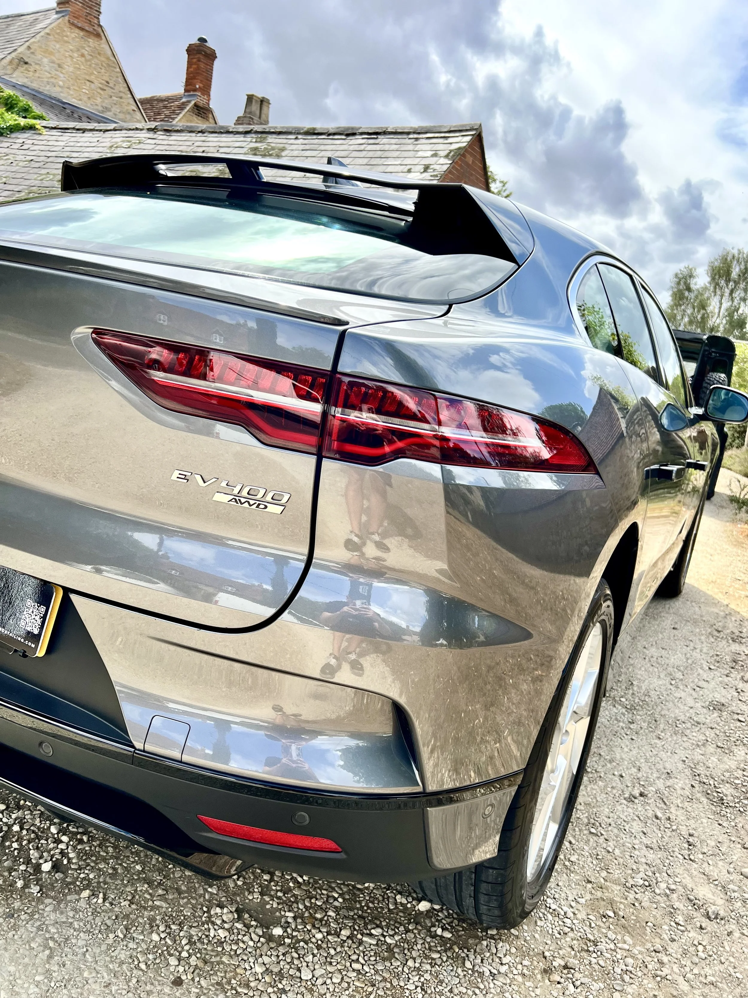 Rear view of a silver electric SUV parked on a gravel surface, with a house and cloudy sky in the background after full mobile valet and detailing.