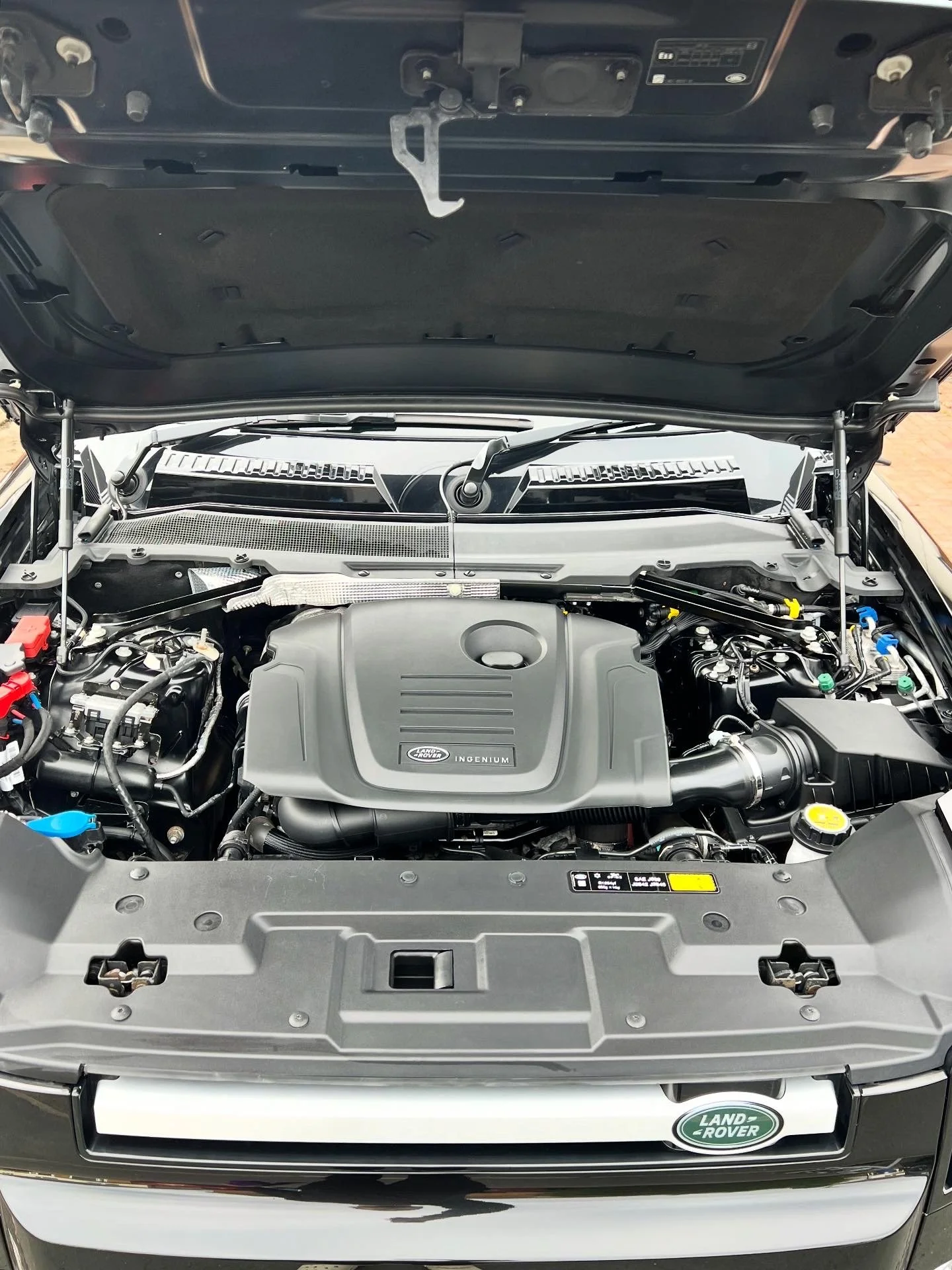 Open engine hood of a Land Rover vehicle showing the engine bay with a cover labeled 'Ingenium' from Jaguar Land Rover after a full engine bay valet.