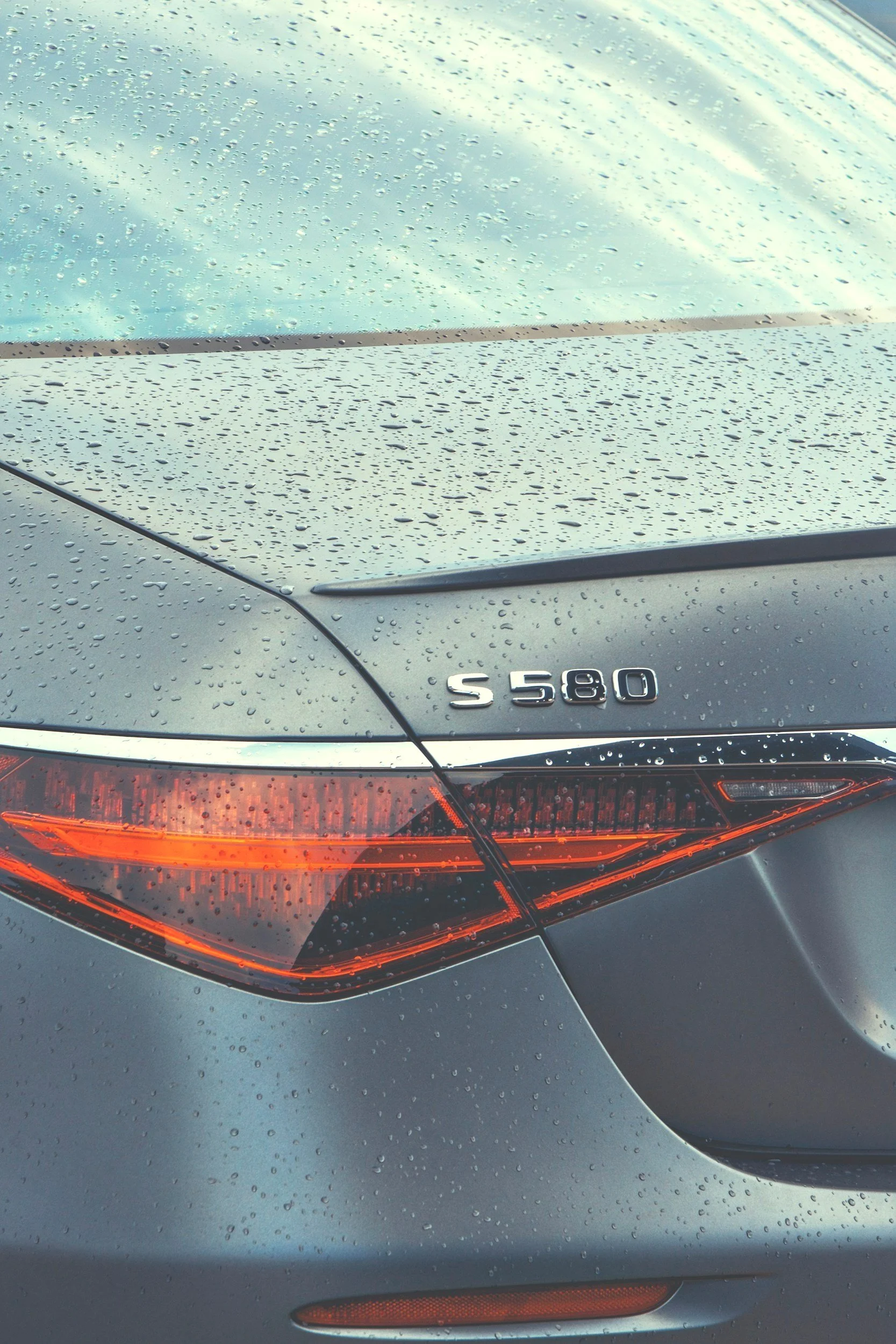 A close-up of the rear of a grey Mercedes-Benz S 580 car with water droplets on the surface after ceramic coating and machine polishing.
