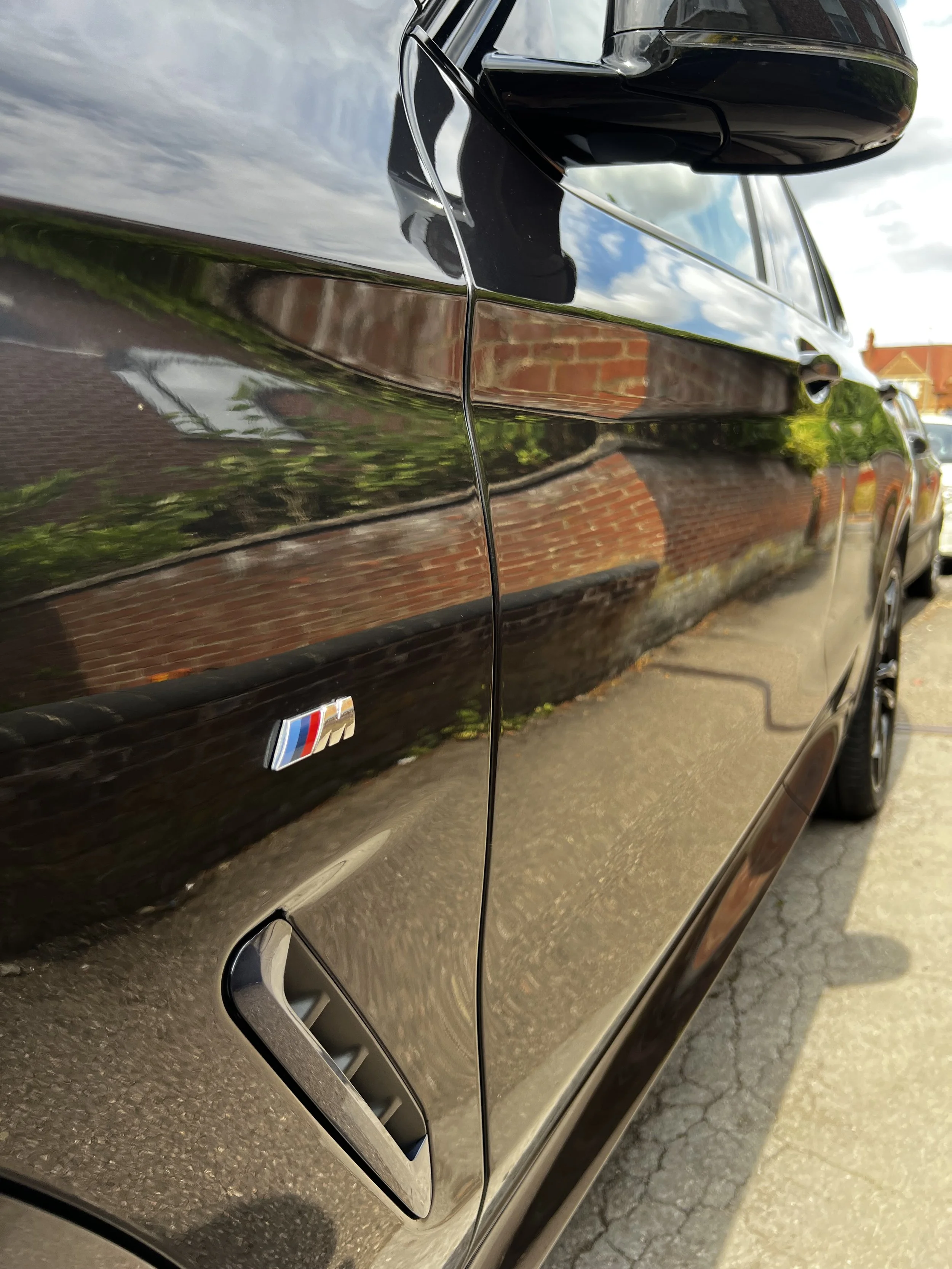 Close-up of a black car's side with a BMW M badge after full valet.