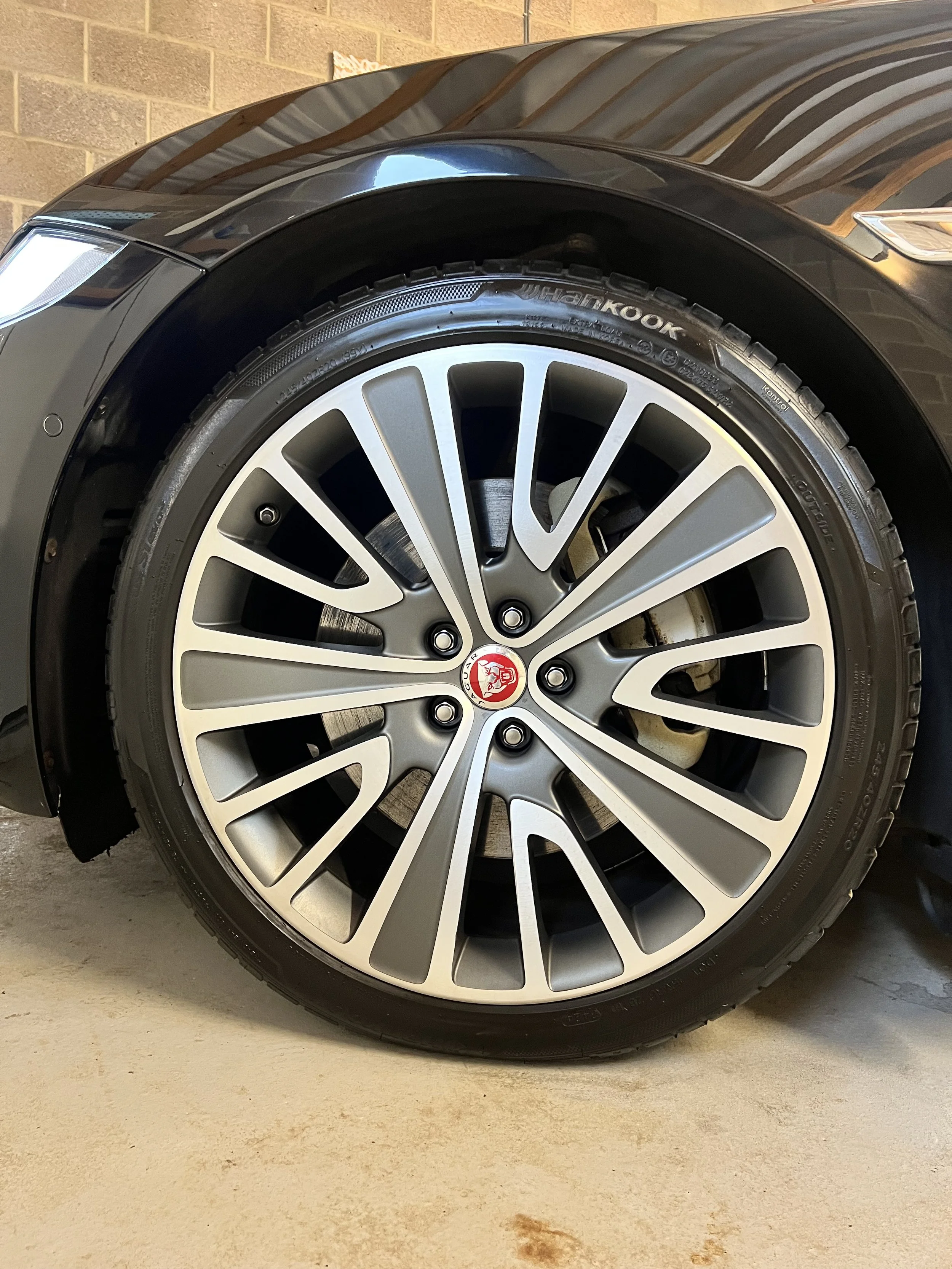 Close-up of a car wheel, featuring a silver alloy rim with multiple spokes and the Jaguar logo at the center, mounted on a black tire with the brand name Hankook visible.