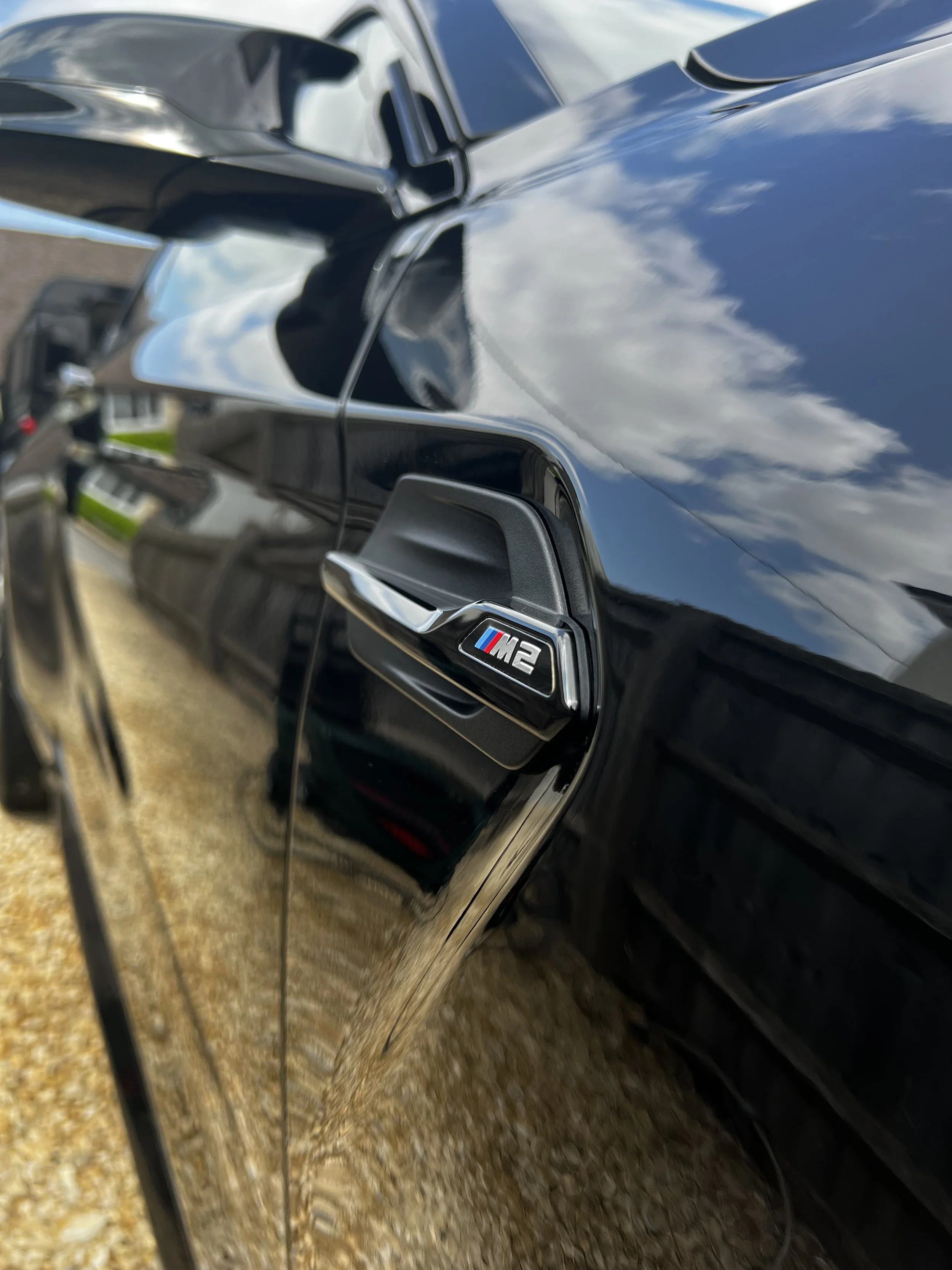 Close-up of a black BMW M2 car showing the M2 badge on the side.