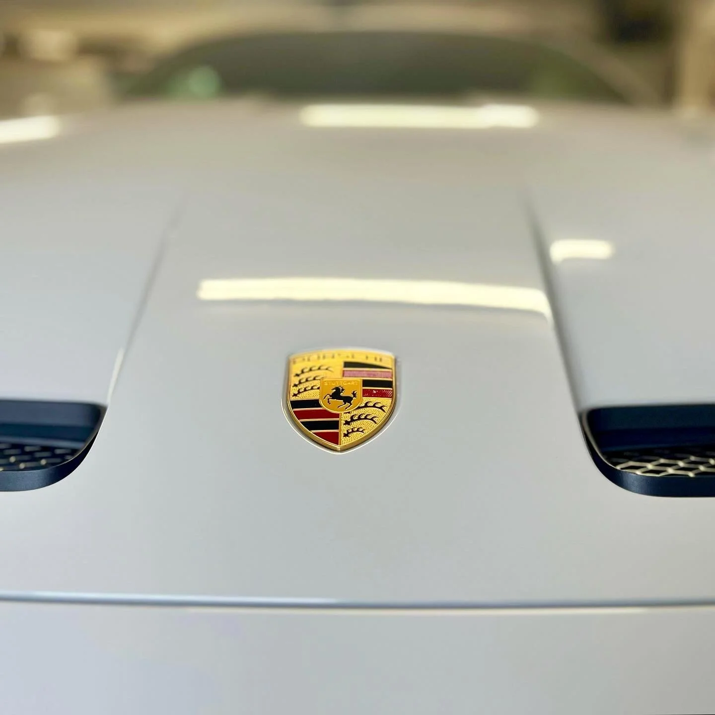 Close-up of a silver Porsche car's hood with the Porsche emblem after a full detail valet by Oxford Car Detailing.