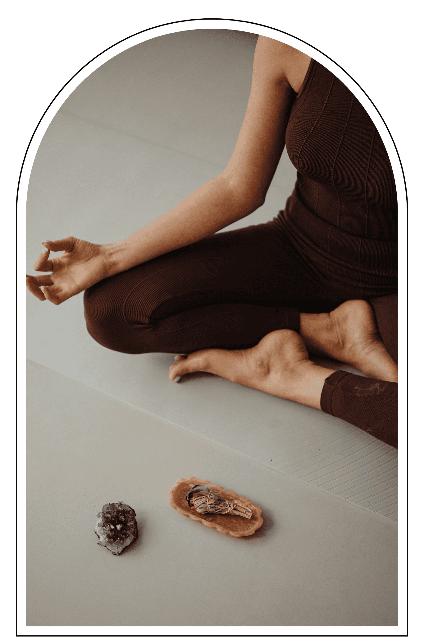 Person in brown workout attire sitting cross-legged on the floor meditating with crystals in front.