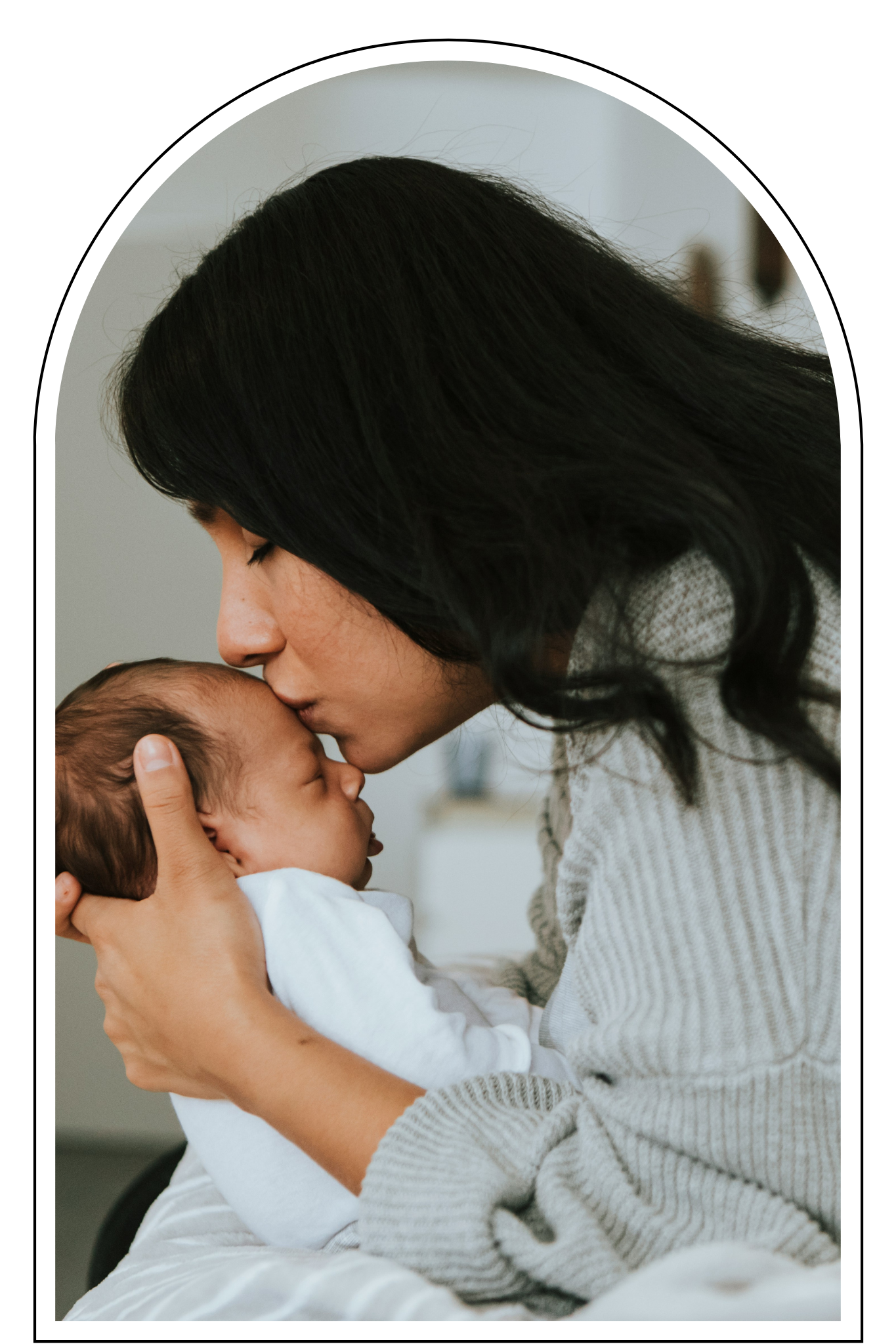 A woman gently holding and kissing a newborn baby on the forehead.