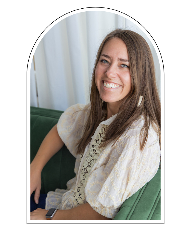 Smiling woman with long brown hair sitting on a green couch with white curtains in the background.