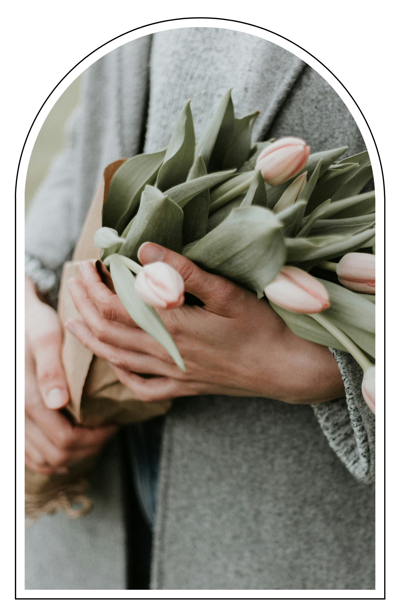 Person holding a bouquet of pink tulips and green leaves wrapped in brown paper