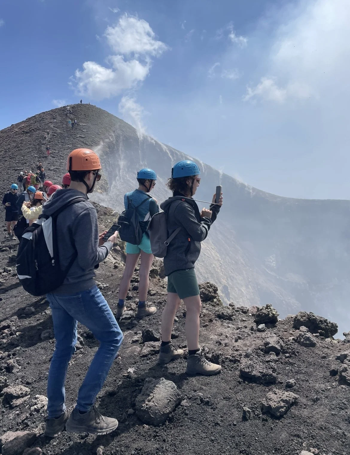Gruppo di persone con caschi protettivi sulla bocca del vulcano, alcune scattando foto e altre ammirando il paesaggio