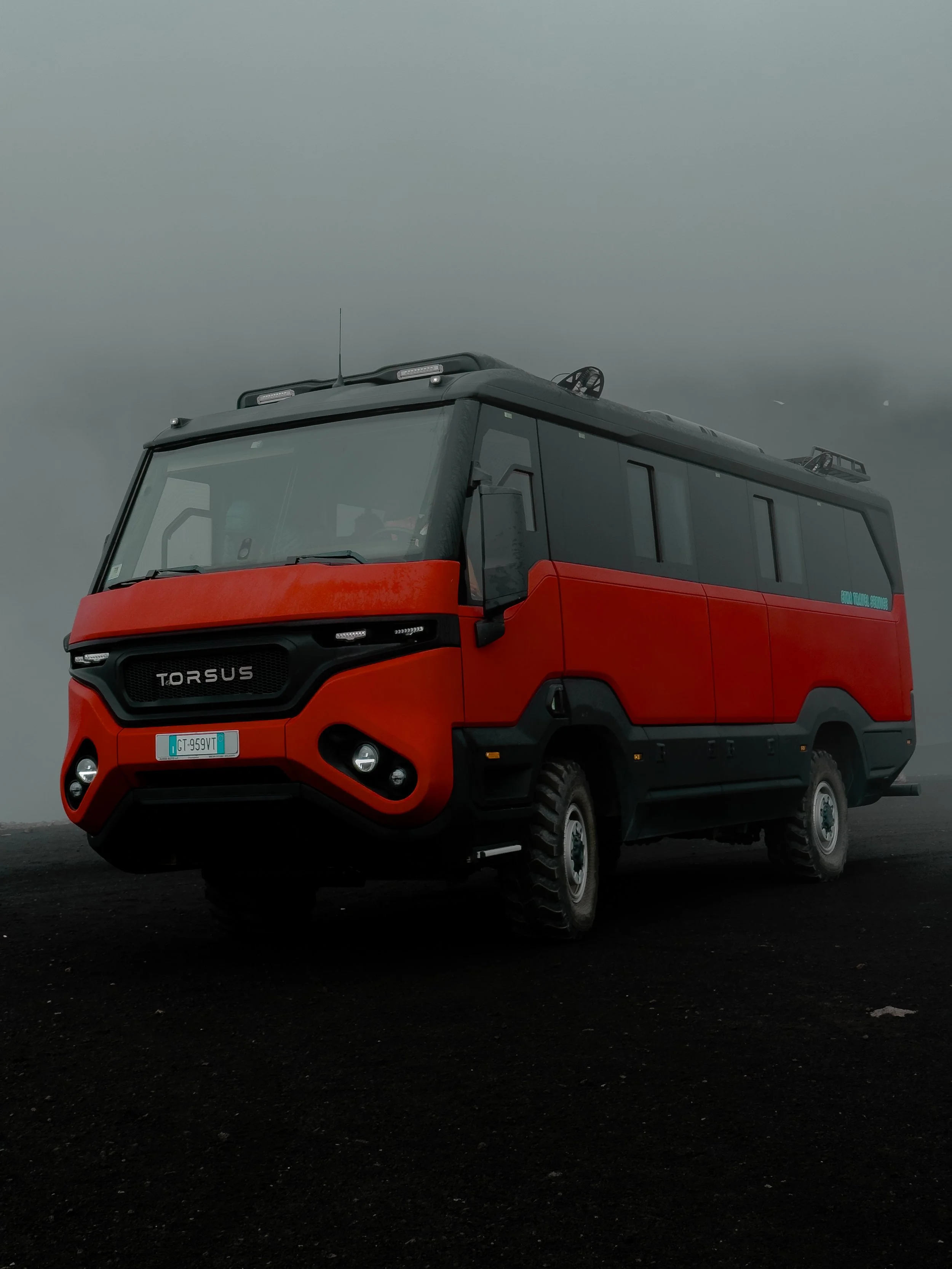 Un camion rosso scuro con dettagli neri e una cabina grande, il tutto su uno sfondo di cielo grigio tempestoso.