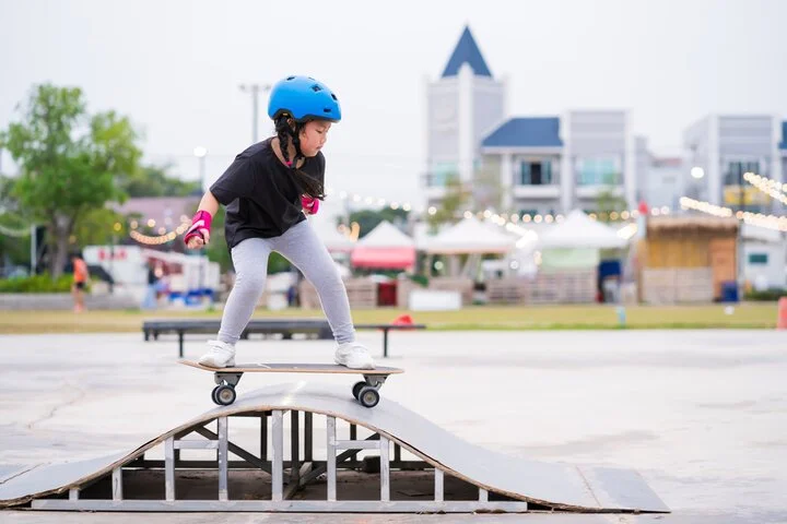 Child wearing a blue helmet practicing skateboarding on a small ramp outdoors.