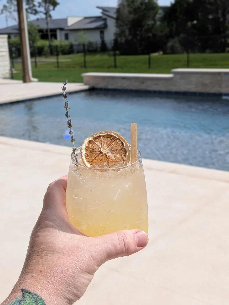 Social Butterfly ATX Lavender Oasis cocktail held poolside in Austin, garnished with a dried citrus wheel, fresh lavender sprig, and a paper straw