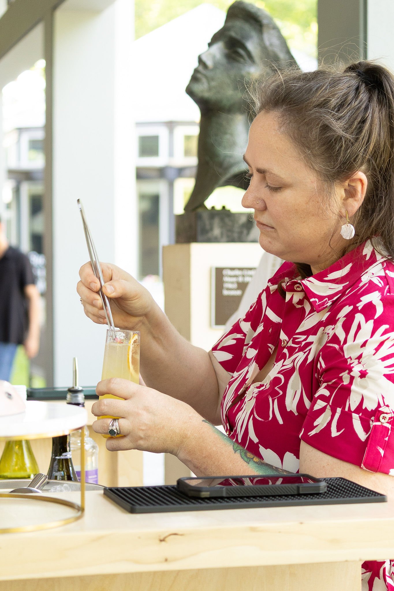 illie Clark of Social Butterfly ATX garnishing a cocktail with a metal straw at an outdoor Austin event