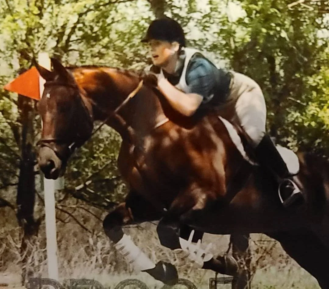 A person riding a brown horse during a nighttime equestrian event, navigating around an orange and white marker, with a background of trees.