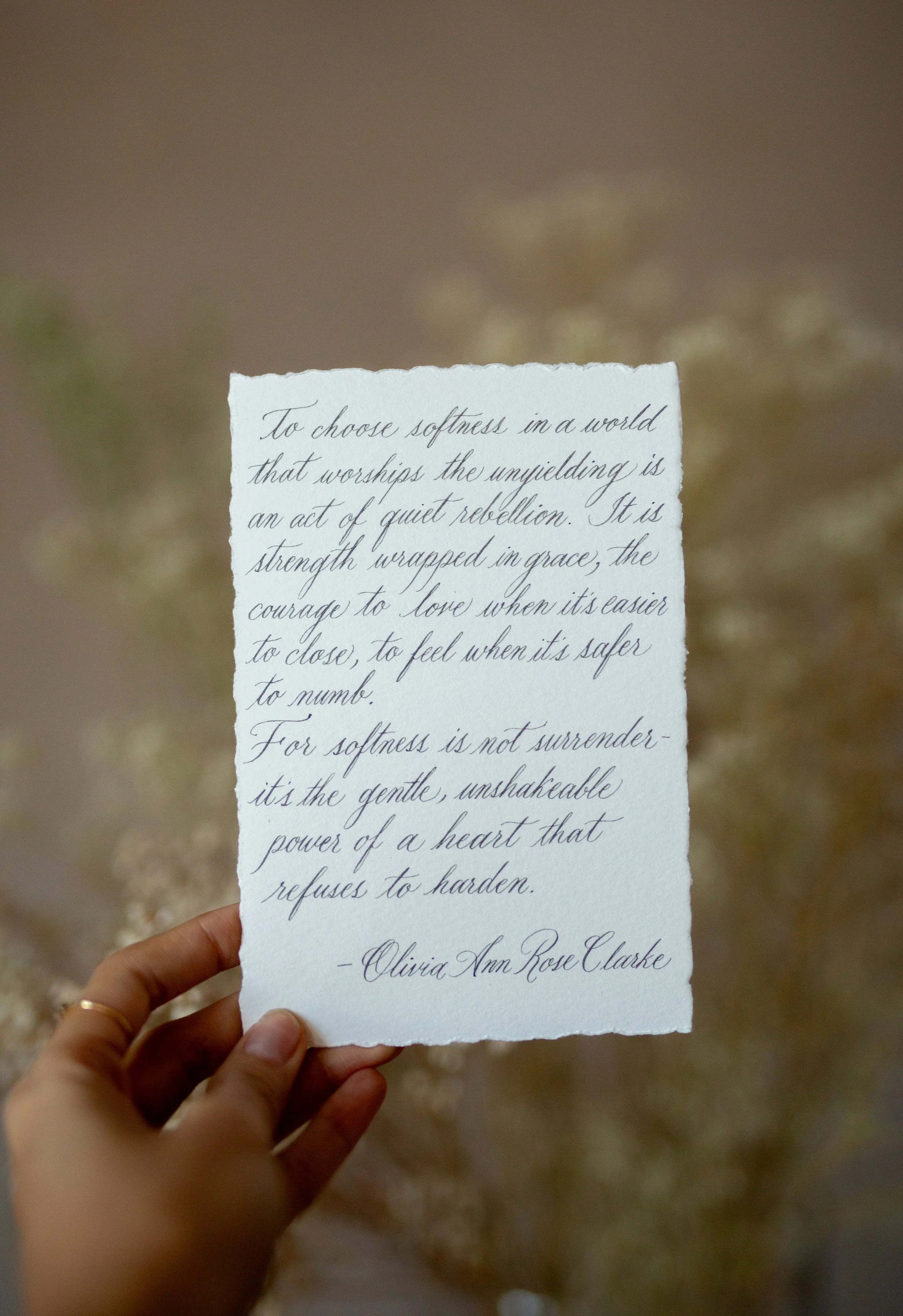 Hand holding a torn paper with a handwritten quote by Olivia Ann Rose Clarke on a blurred background.