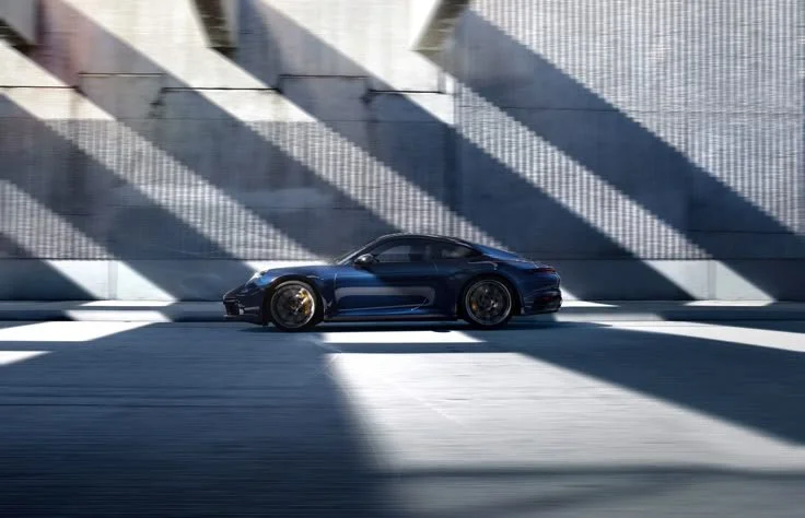 A sleek, black sports car parked on a road with dramatic shadows cast by a nearby structure.