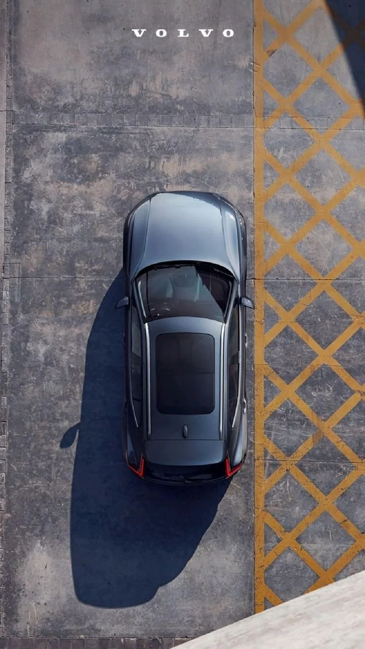 Top-down view of a gray car parked in a parking lot near a yellow striped crosshatched area.