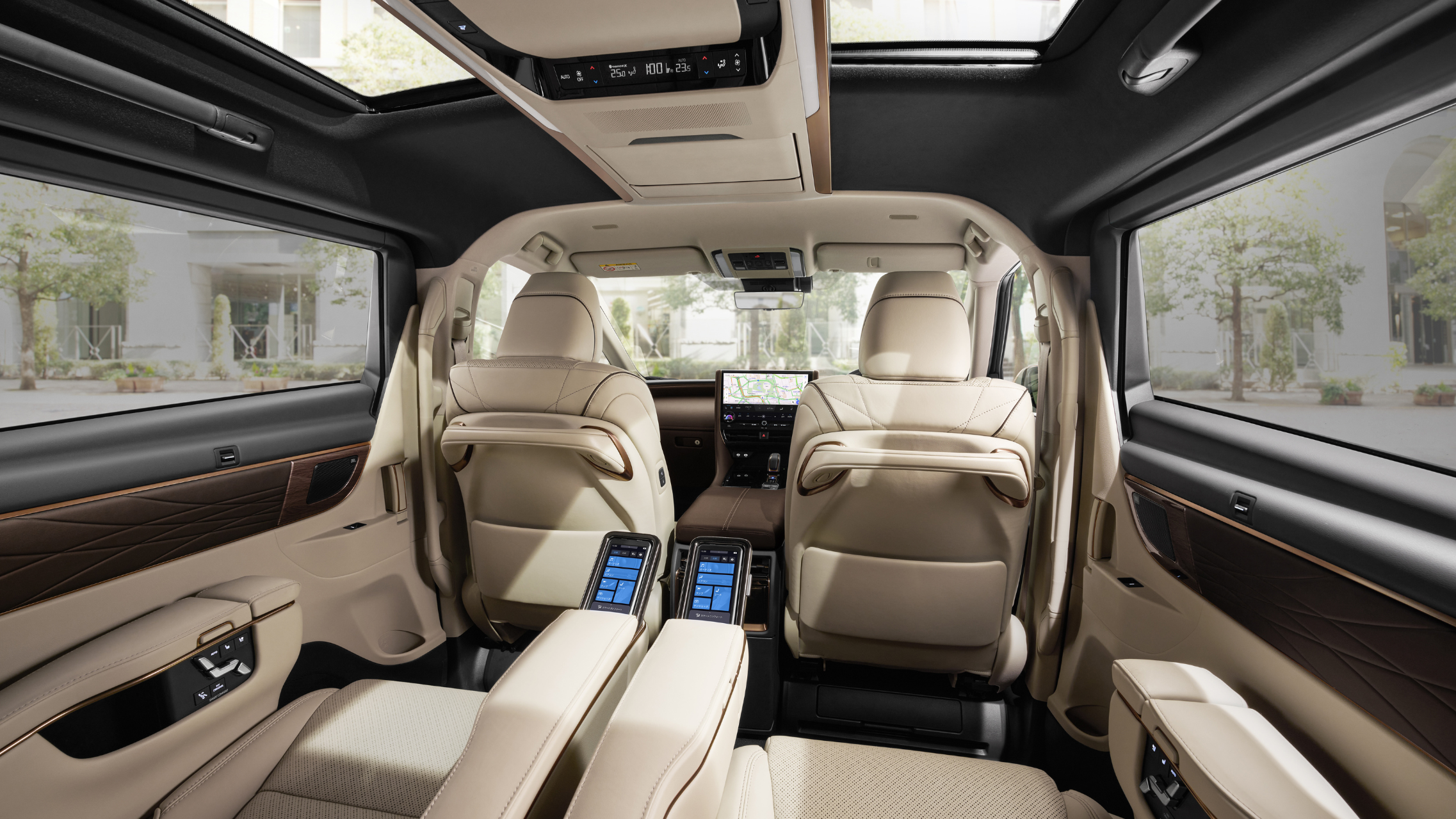Interior view of a luxury van with beige leather seats, a central control panel, and large panoramic windows showing trees outside.