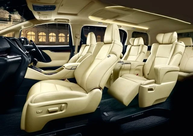 Interior of a luxury van with beige leather seats, some of which are captain's chairs, seen from the passenger side.