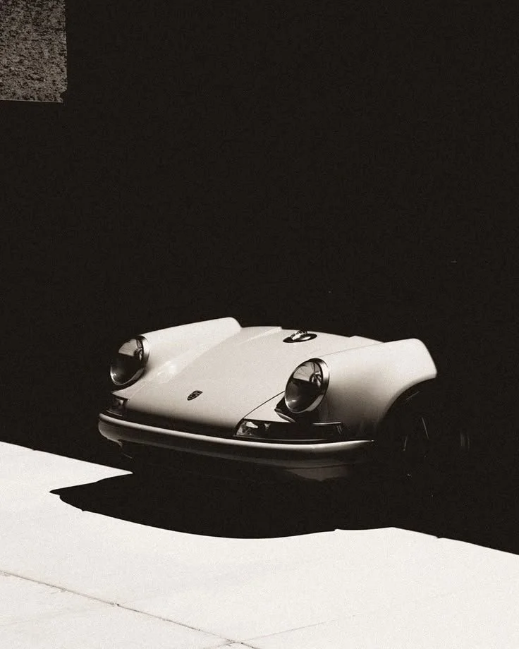 A vintage silver Porsche 911 sports car parked on a surface with a stark black background