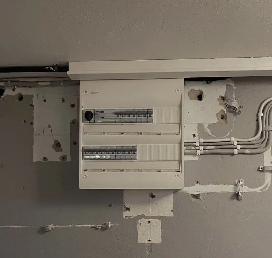 Elcentral på en vägg, med ledningar och hål runtom, i ett kvarter under installation eller renovering. Bra och säker elcentral!